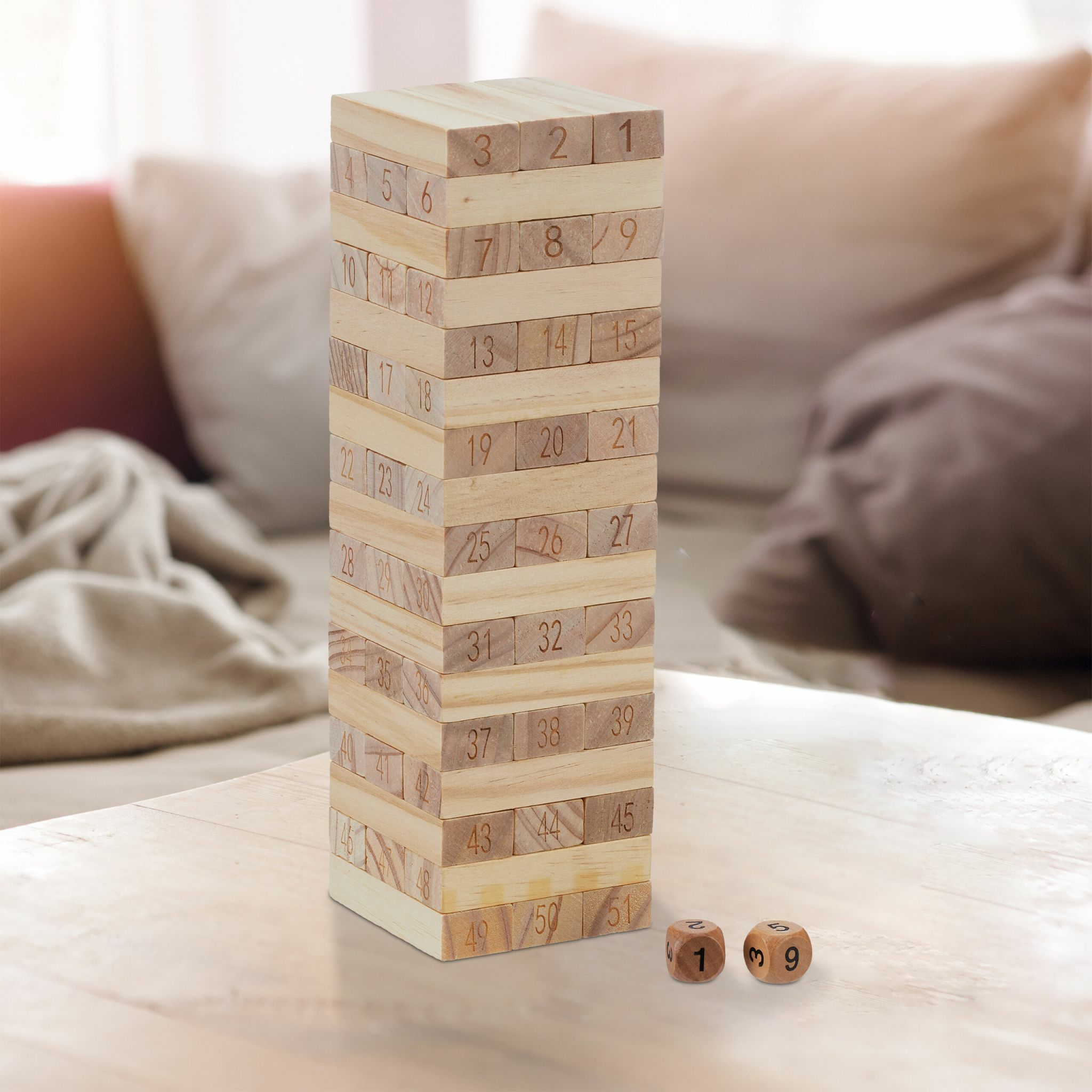 Ein hölzernen Stapelturm mit nummerierten Klötzen und zwei Würfeln auf einem Tisch vor einem Sofa.