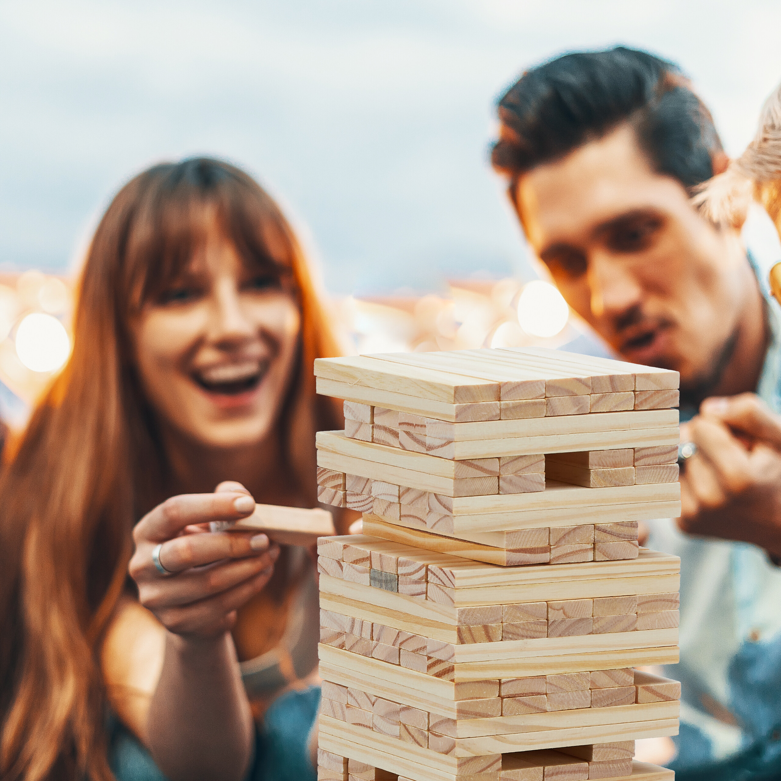 Freunde spielen Jenga, eine Frau lächelt, während sie einen Block aus dem Turm zieht.