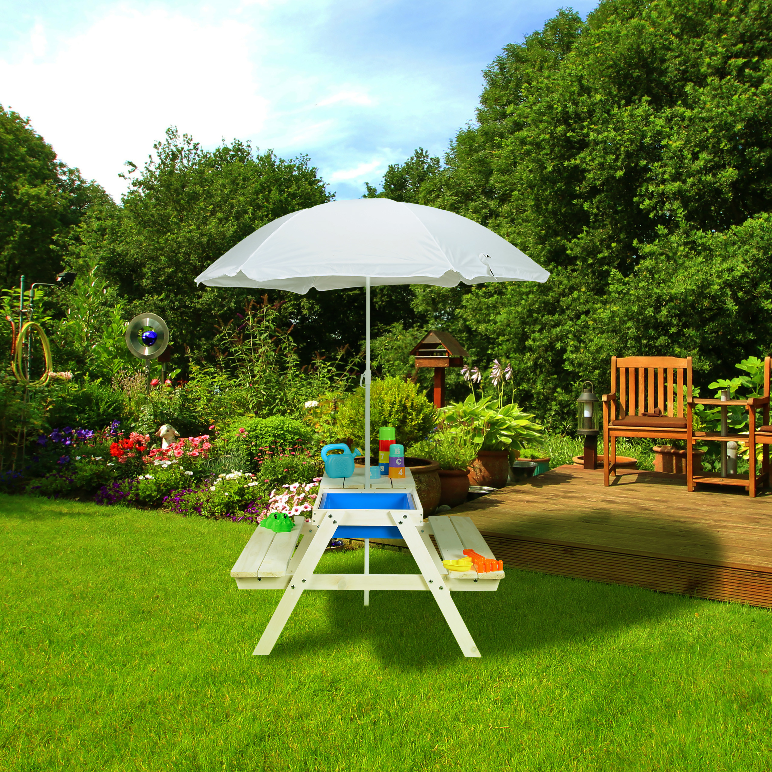 Ein weißer Kindertisch mit Sonnenschirm steht auf einem grünen Rasen in einem sonnigen Garten.