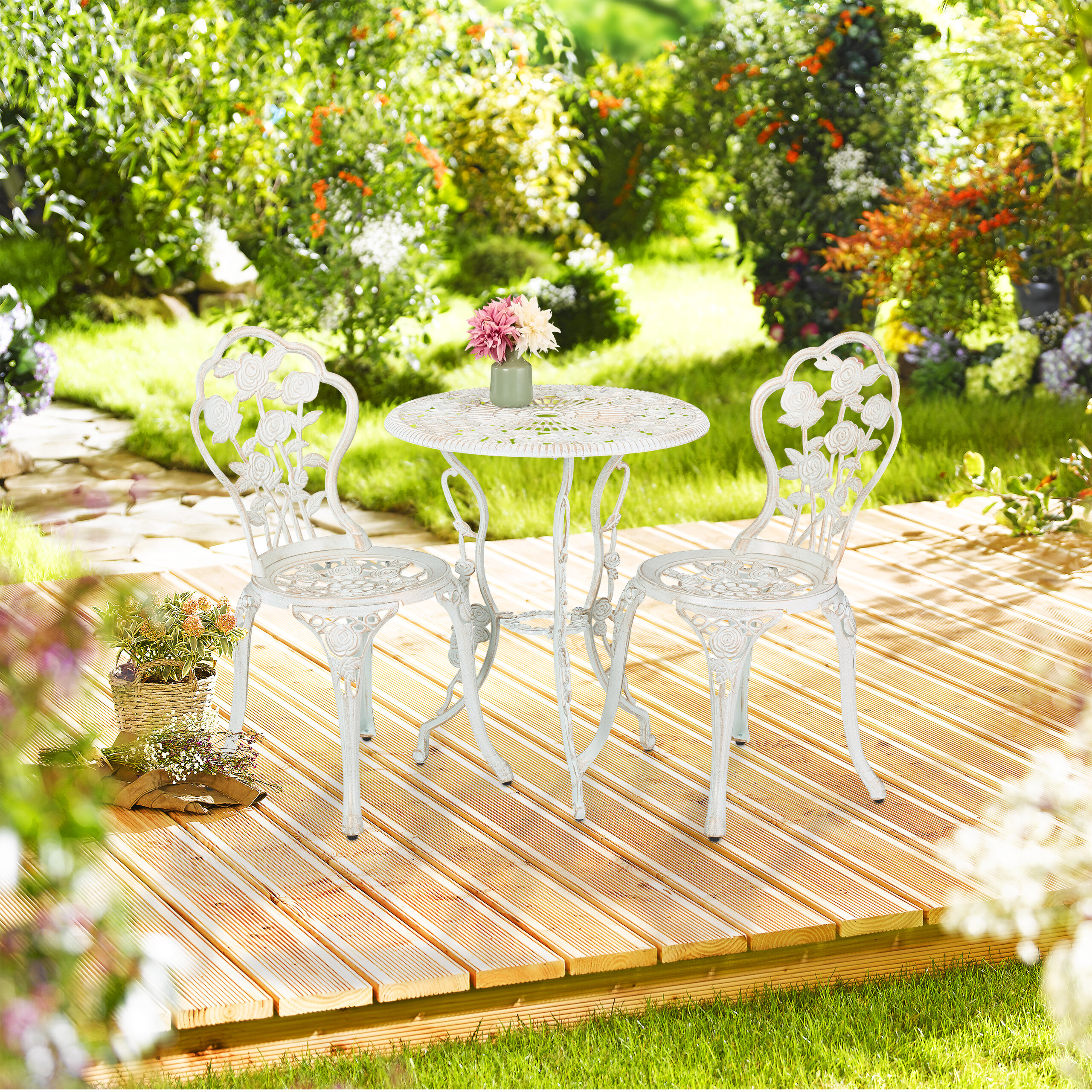 Weiße Metallgartenmöbel mit Tisch und zwei Stühlen auf einer Holzterrasse im Garten.