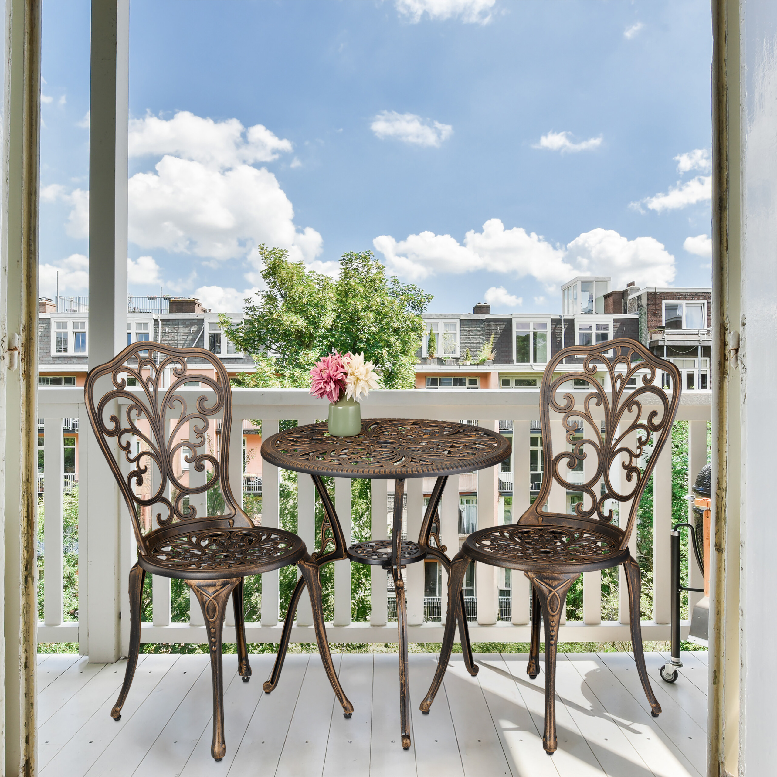 Balkon mit zwei gusseisernen Stühlen, rundem Tisch, Blumenvase und Stadtblick unter blauem Himmel.
