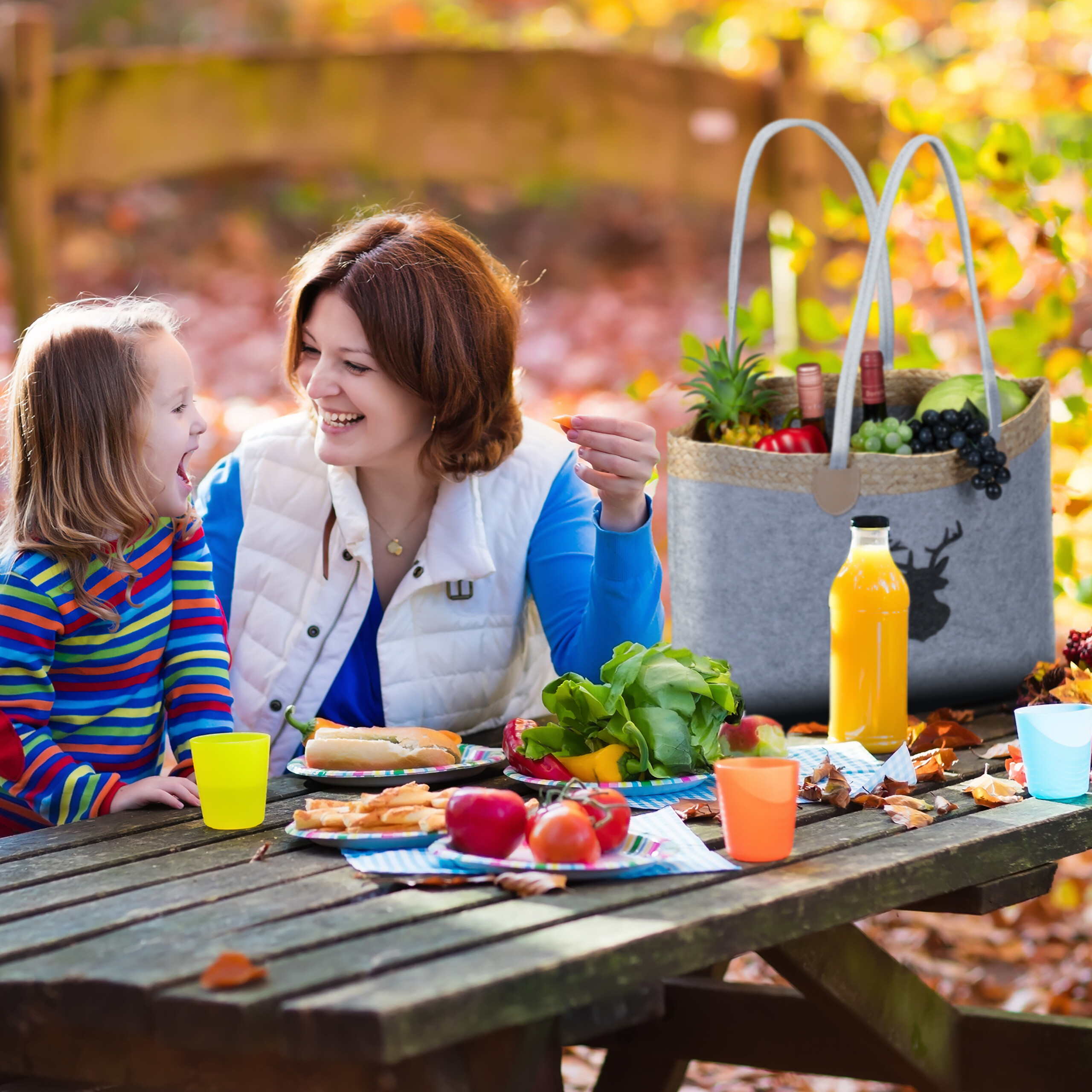 Eine Frau und ein Kind picknicken im Herbstwald am Holztisch.