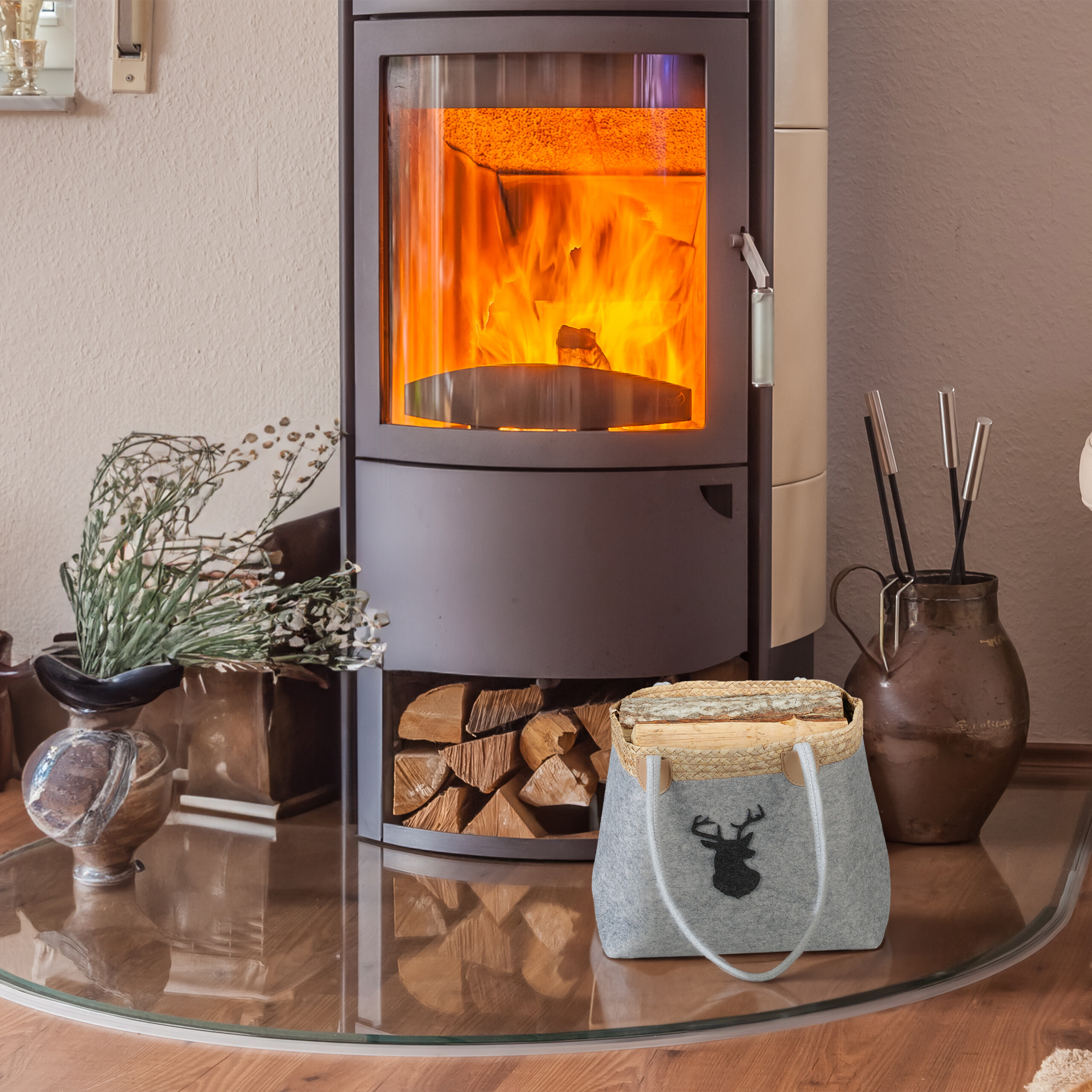 Ein brennender Kaminofen steht auf einer Glasplatte, daneben liegen Holzscheite und Deko.