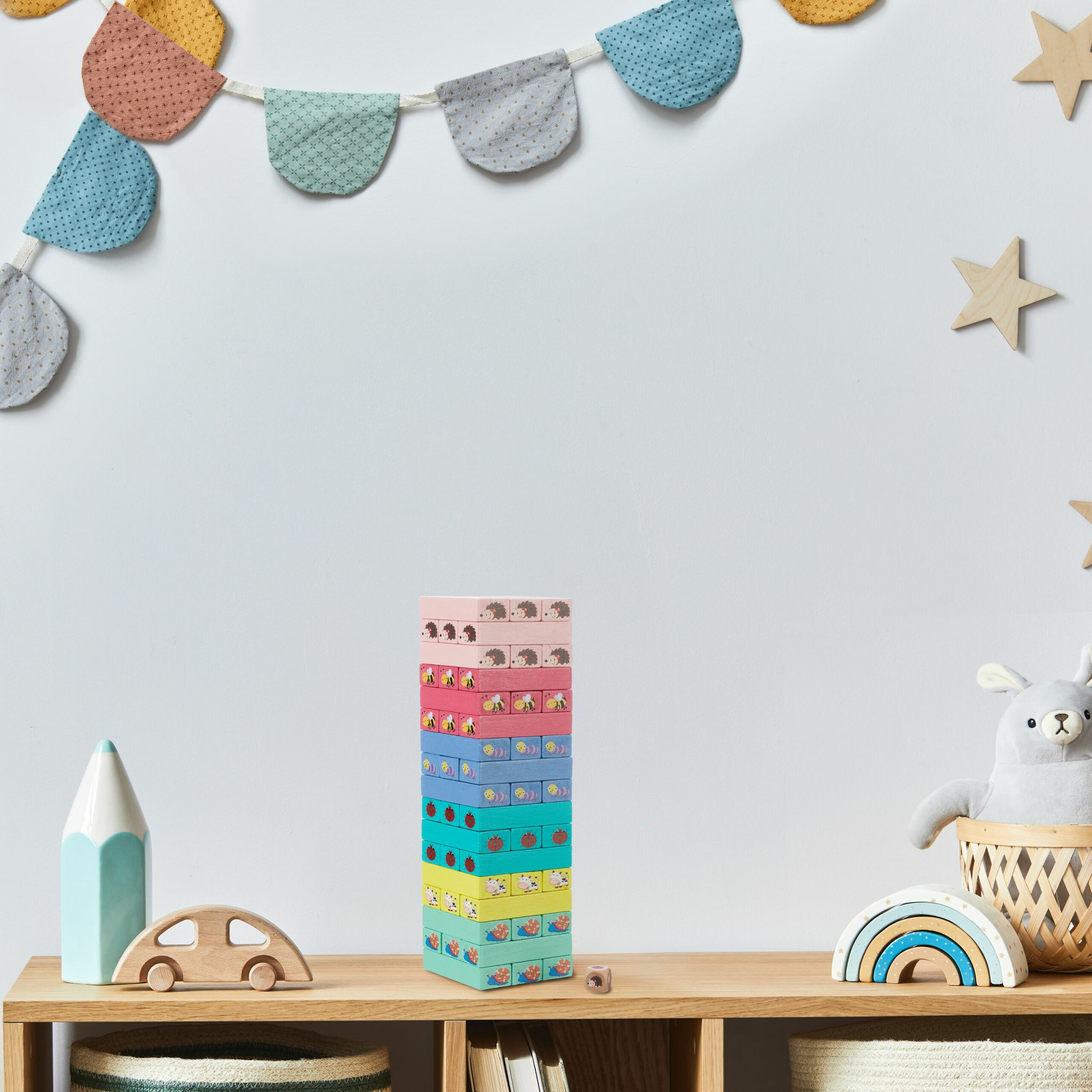 Holzregal mit buntem Stapelturm, Spielzeugauto, Regenbogen und Stofftier. Bunte Wimpelkette und Holzsterne an der Wand.