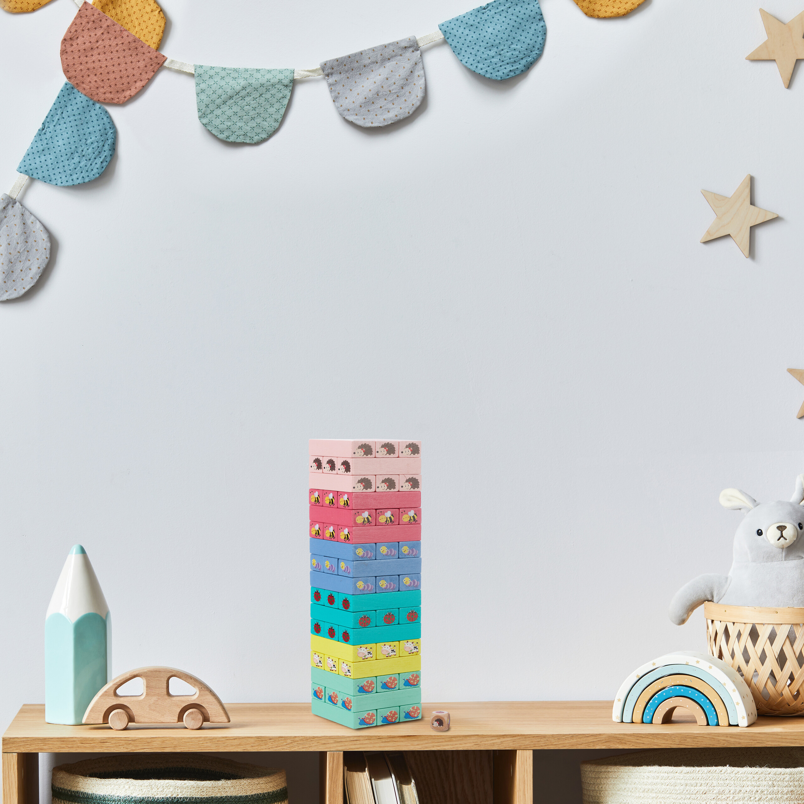 Holzregal mit buntem Turm, Stofftier, Regenbogen, Holzigel und Wimpelkette an der grauen Wand.