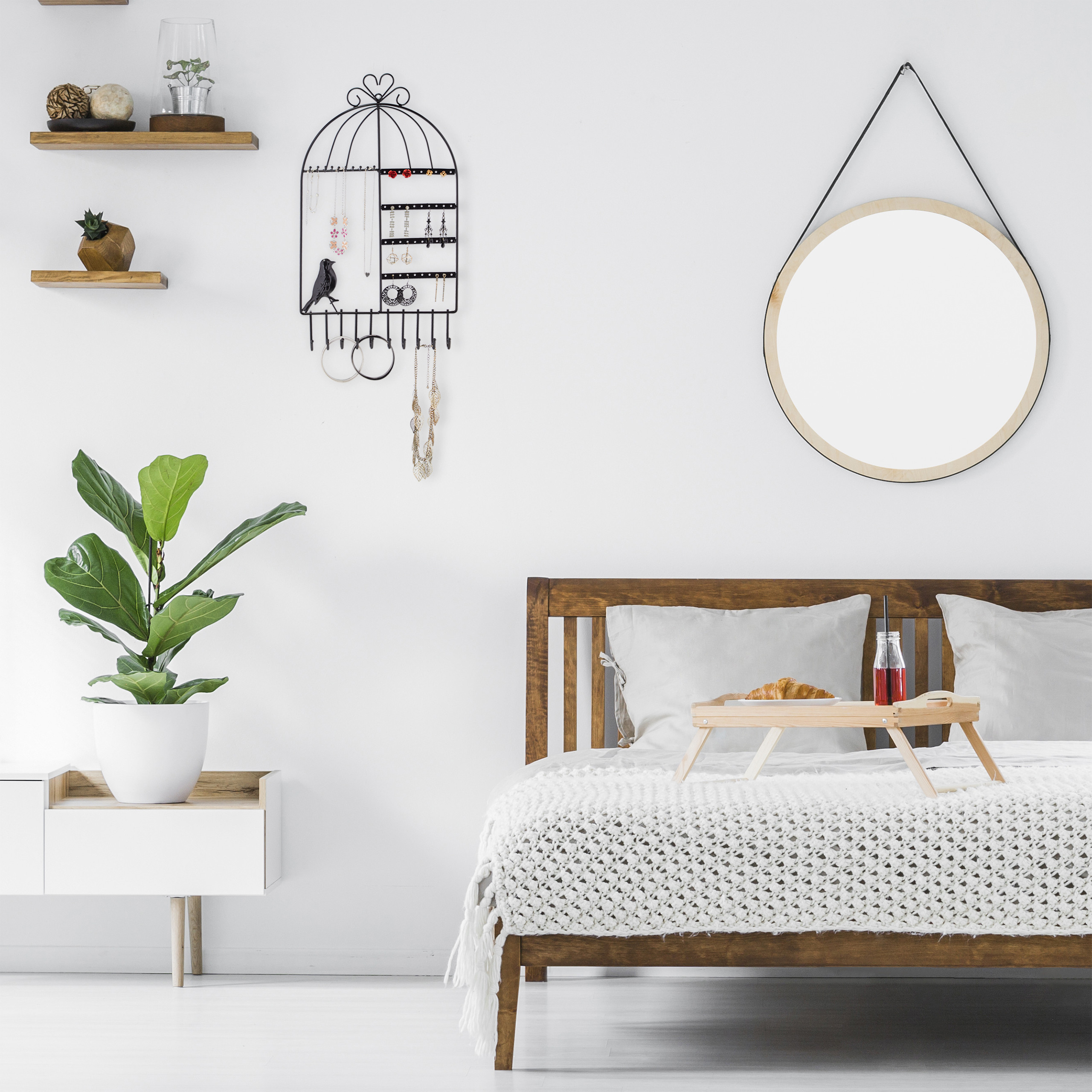 Ein weißes Schlafzimmer mit Holzbett, runden Spiegel, Wandregalen und einem Frühstückstablett auf dem Bett.