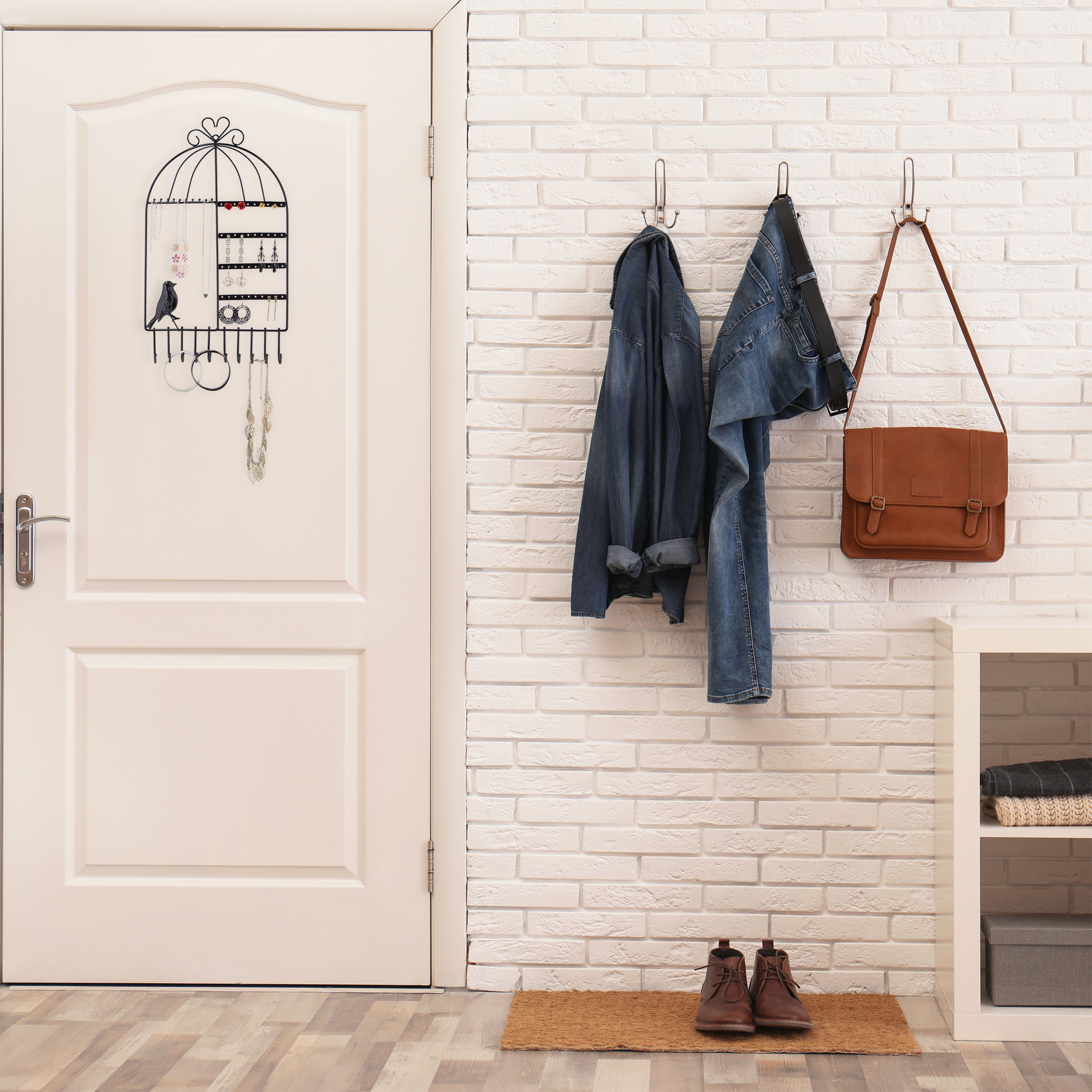 Flur mit weißer Ziegelwand, heller Tür mit Schmuckhalter, Kleiderhaken mit Jacke, Jeans, Tasche und Schuhen.