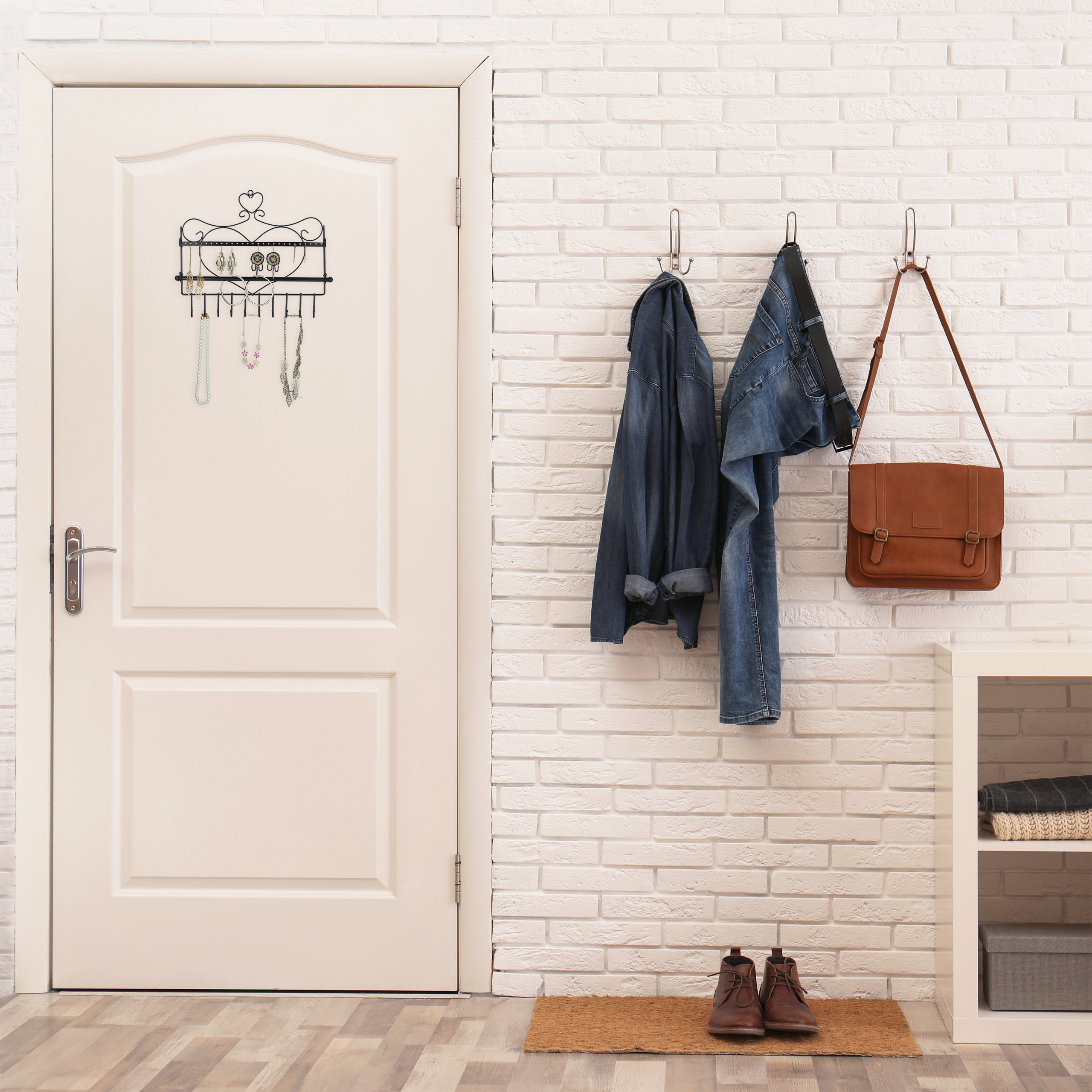 Weiße Ziegelwand mit Garderobenhaken für Jacke, Jeans und Tasche, daneben eine weiße Tür mit Schmuckhalter.