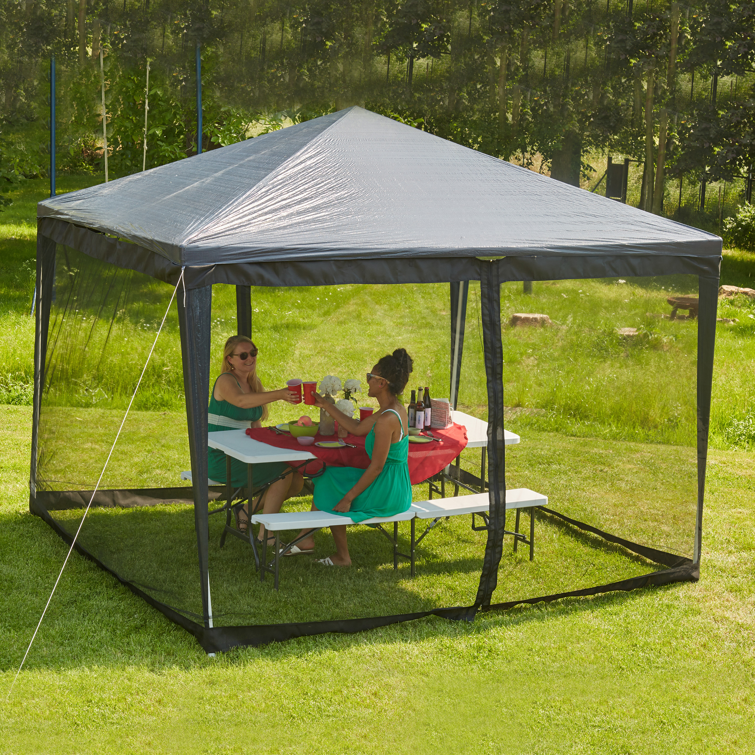Zwei Frauen sitzen im Freien unter einem schwarzen Pavillon an einem gedeckten Tisch.