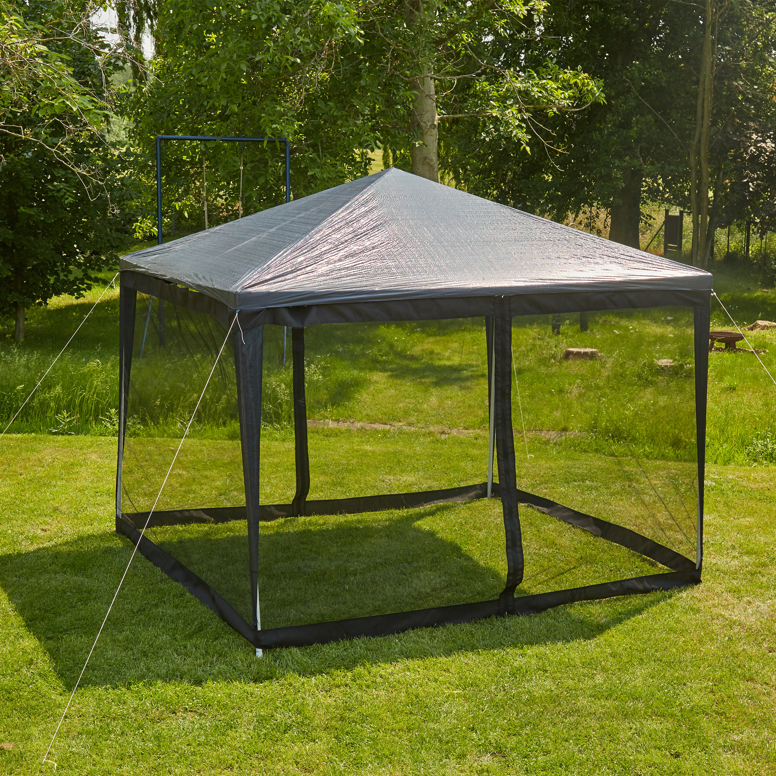 Ein grauer Pavillon mit schwarzen Netzwänden auf einem Rasen, umgeben von Bäumen.