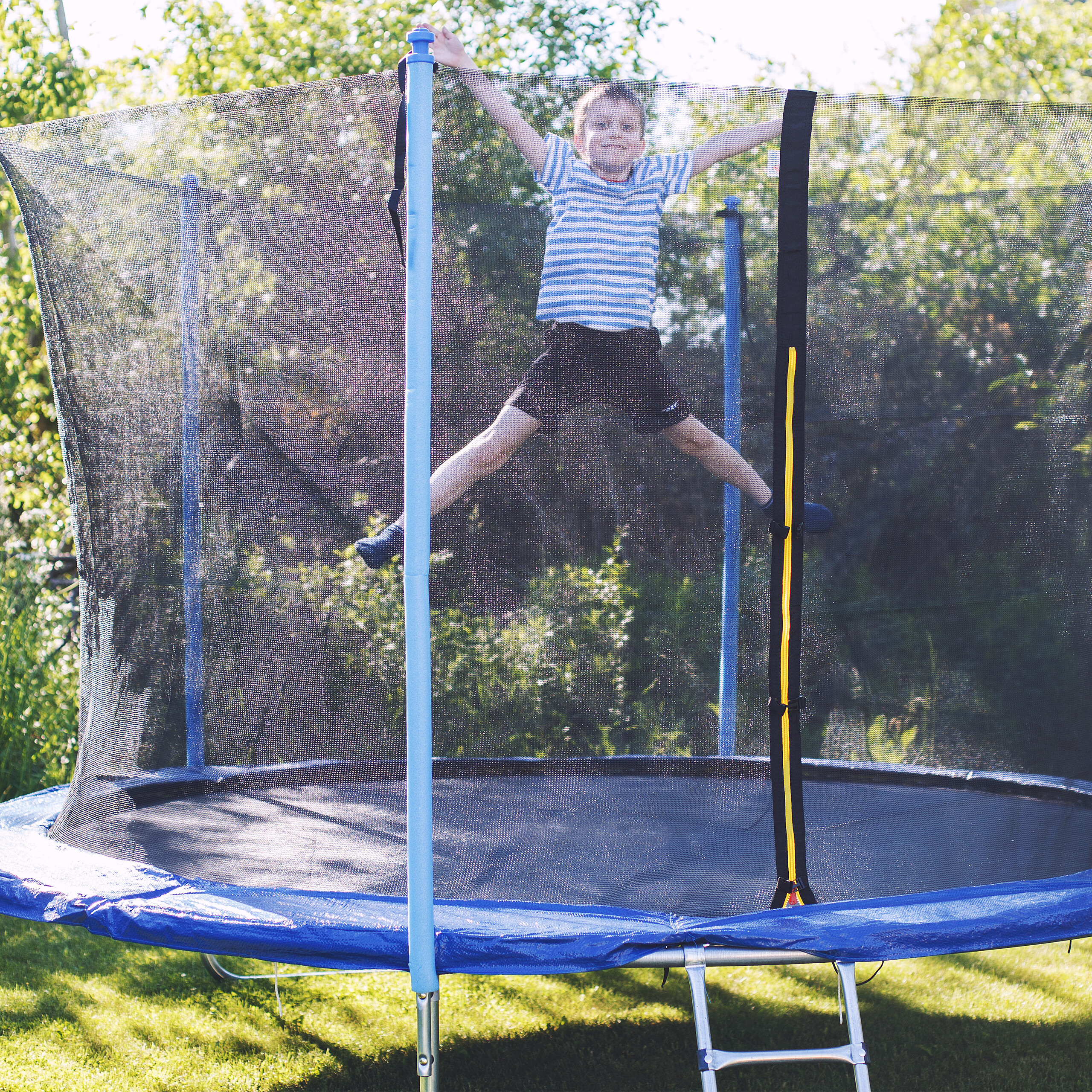 Ein Junge springt in der Luft auf einem Trampolin mit Netz im Garten.