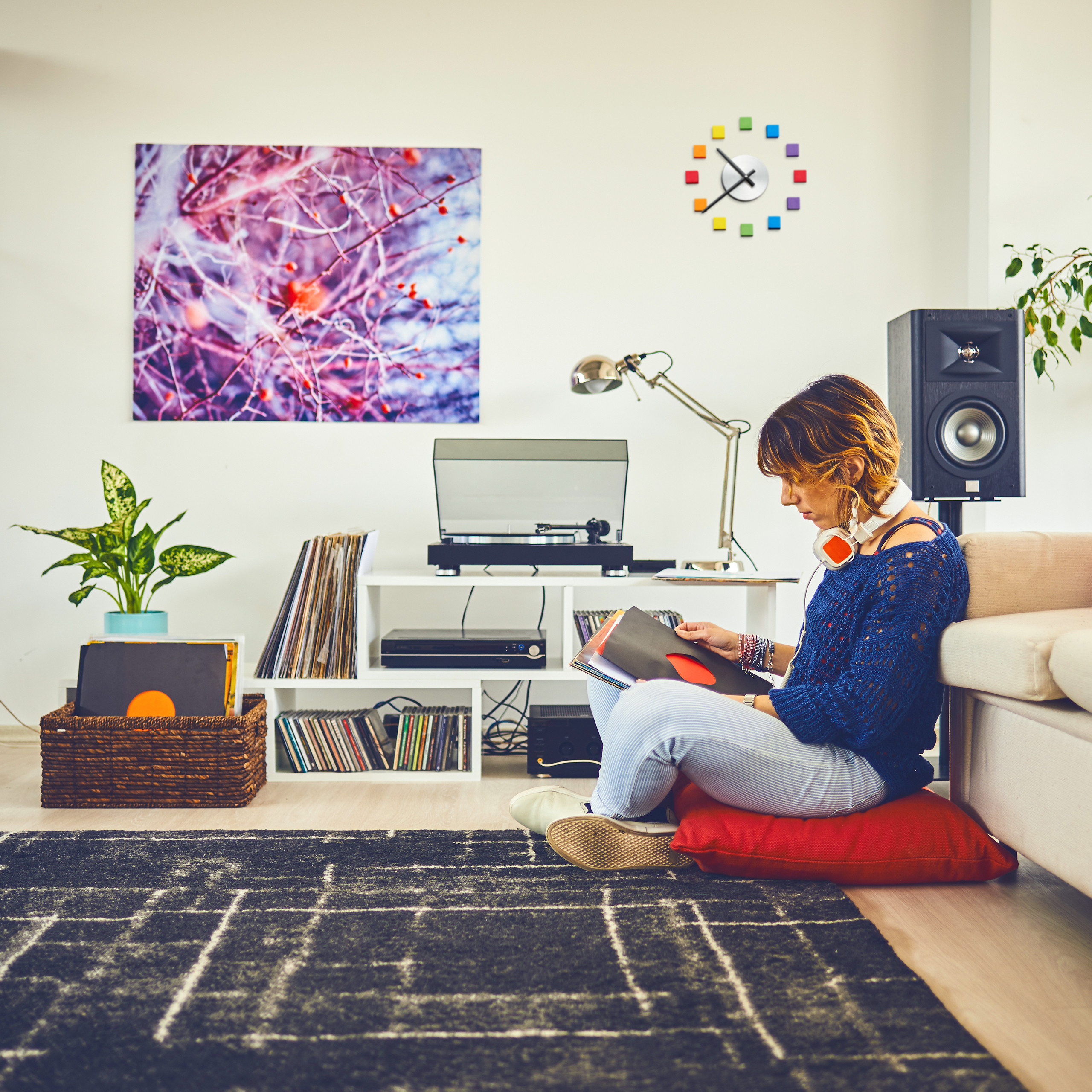 Eine Frau sitzt auf einem roten Kissen im Wohnzimmer und sortiert Schallplatten.