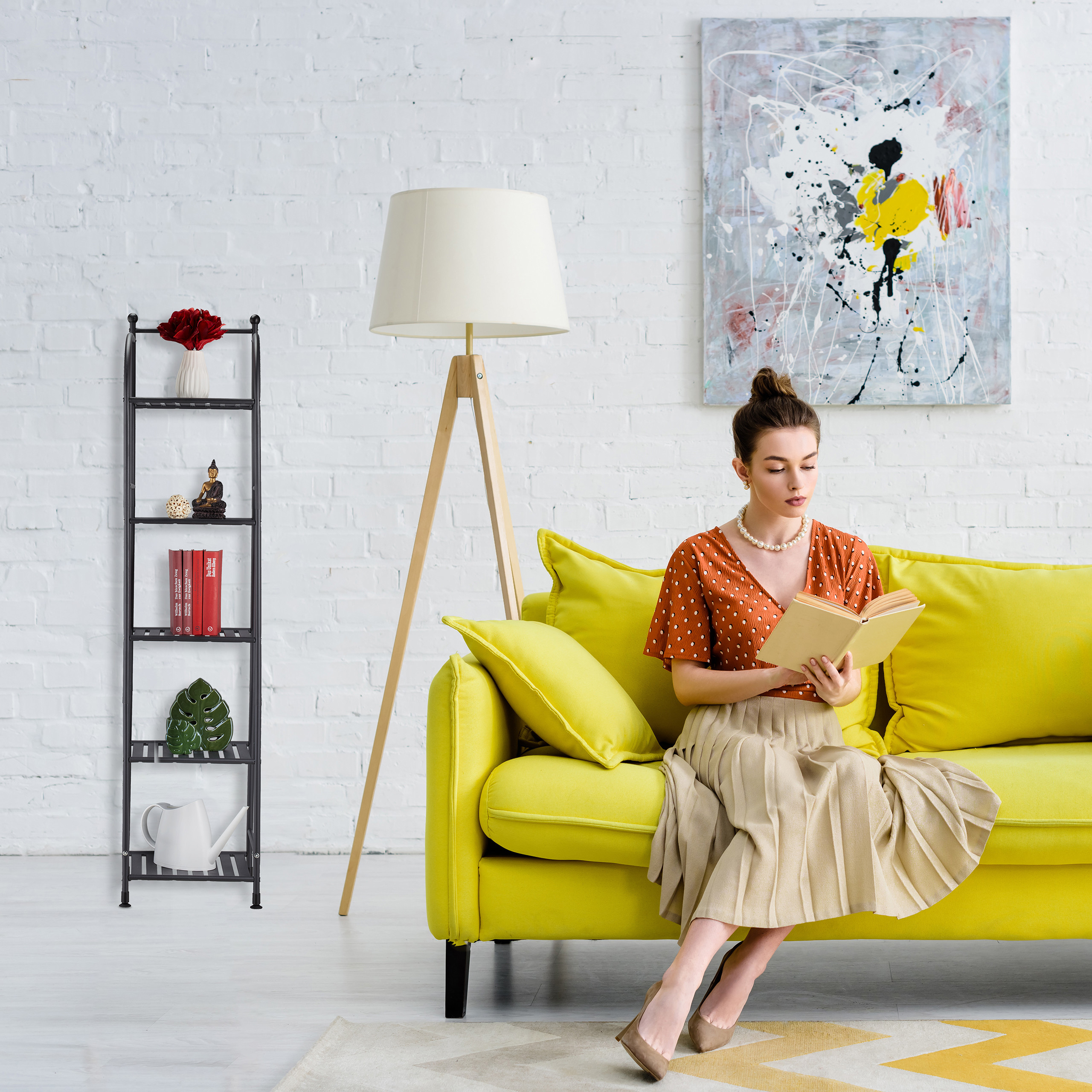 Eine Frau in einem orangefarbenen Oberteil liest ein Buch auf einem gelben Sofa in einem hellen Raum mit gemaltem Bild.