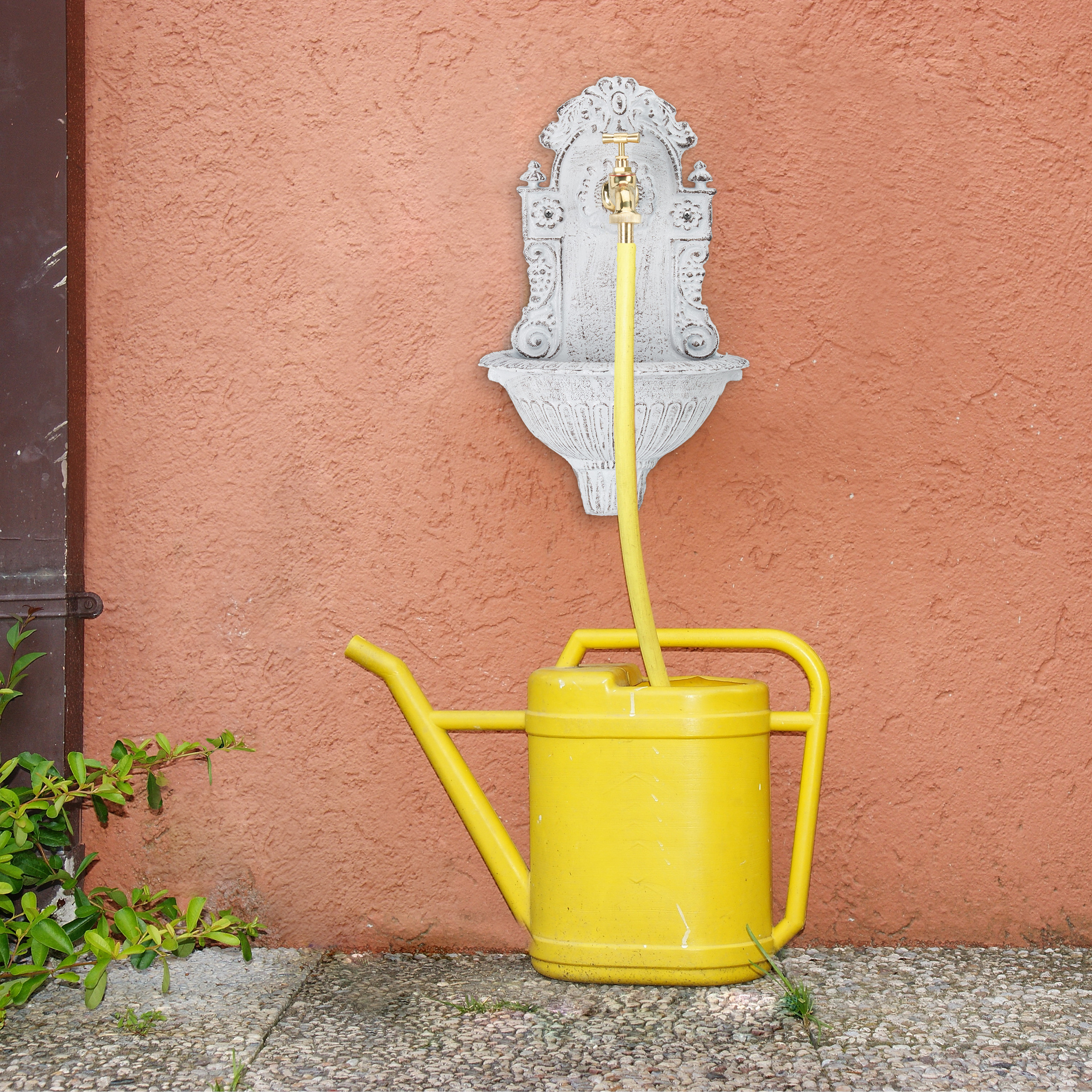 Ein gelber Schlauch verbindet einen Wandbrunnen mit einer gelben Gießkanne vor einer orangefarbenen Wand.