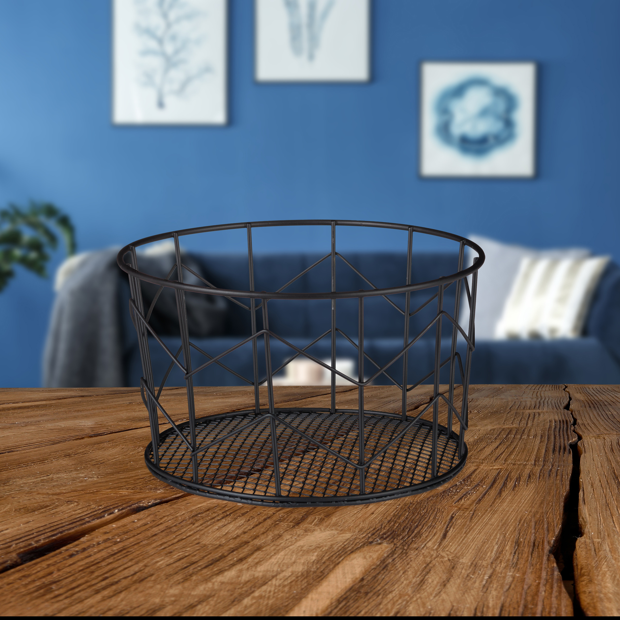 Ein schwarzer Drahtkorb steht auf einem Holztisch vor einer blauen Wand in einem Zimmer.