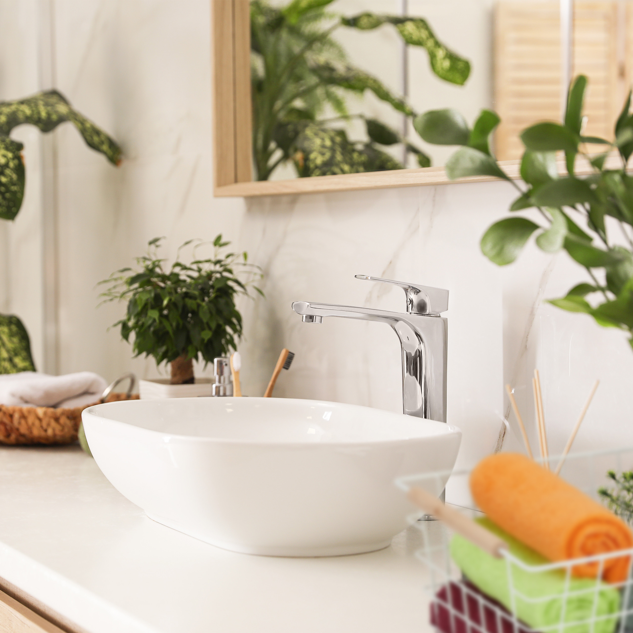 Ein weißes Waschbecken mit Chromarmatur auf einer Arbeitsplatte, umgeben von grünen Pflanzen und Handtüchern.