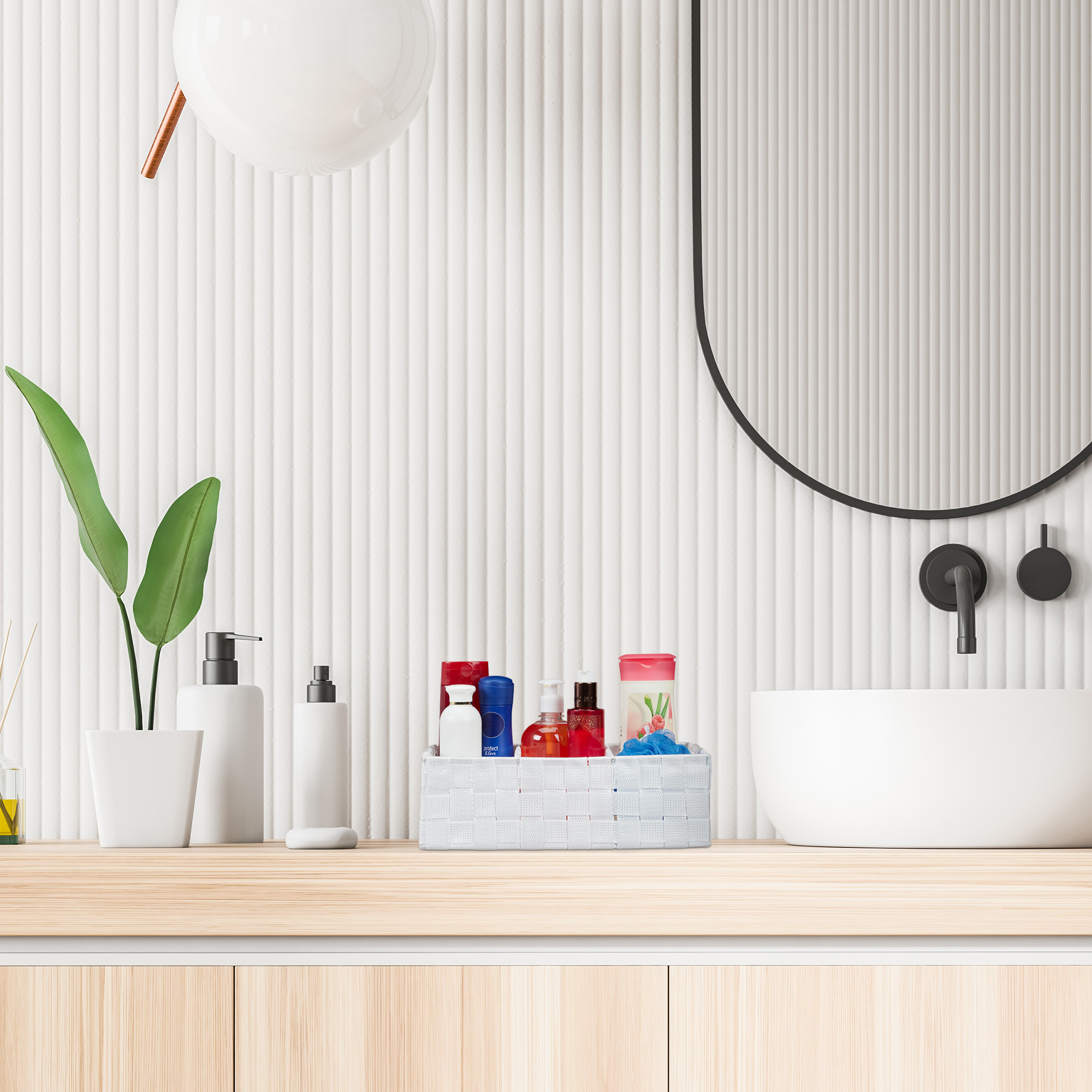 Ein weißes Badezimmer mit Holzarbeitsplatte, Waschbecken, Badutensilien im Korb, Pflanze, Spiegel und runder Lampe.