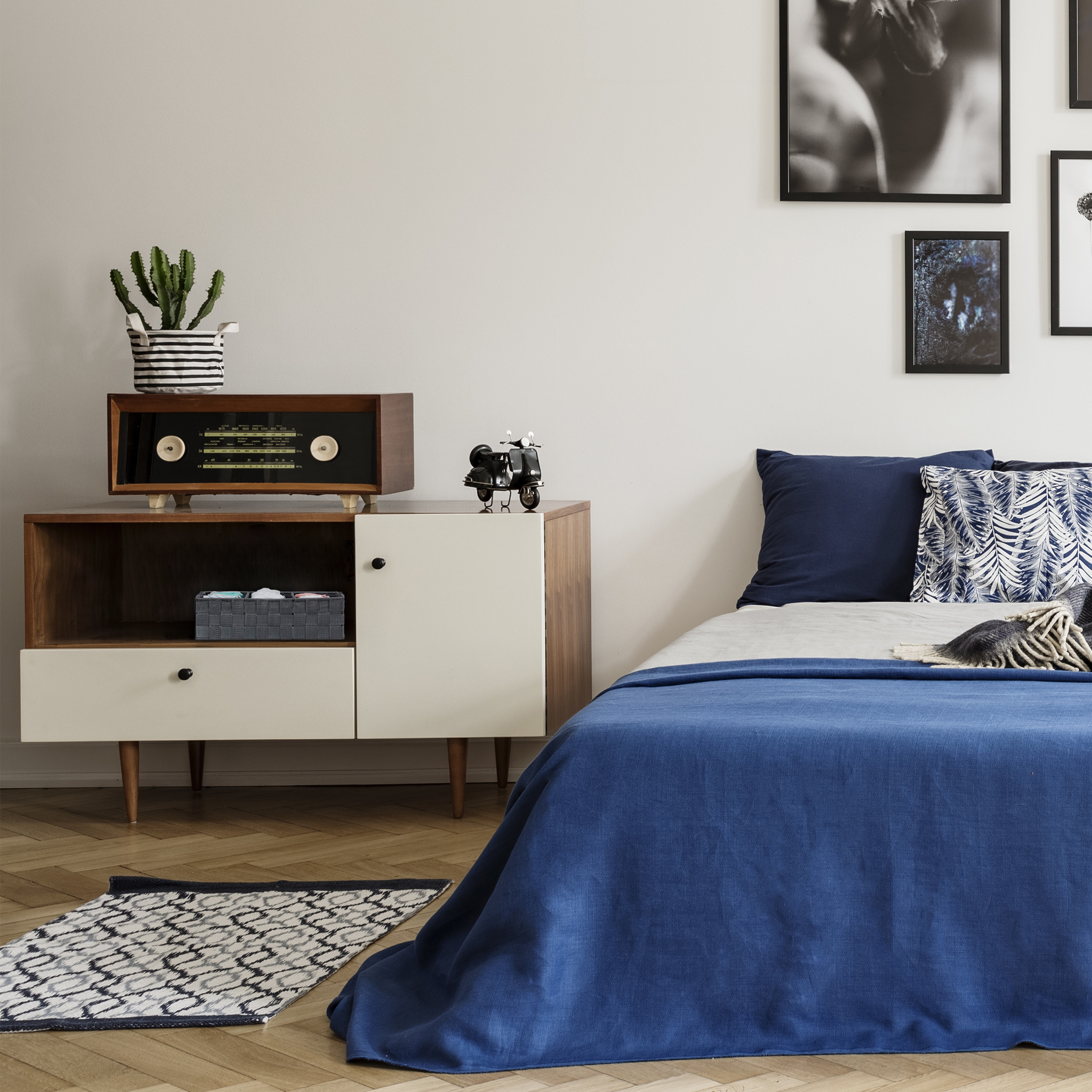 Ein Schlafzimmer mit Retroschrank, Vintage-Radio, Kaktus, blauer Bettwäsche und Schwarz-Weiß-Kunst.