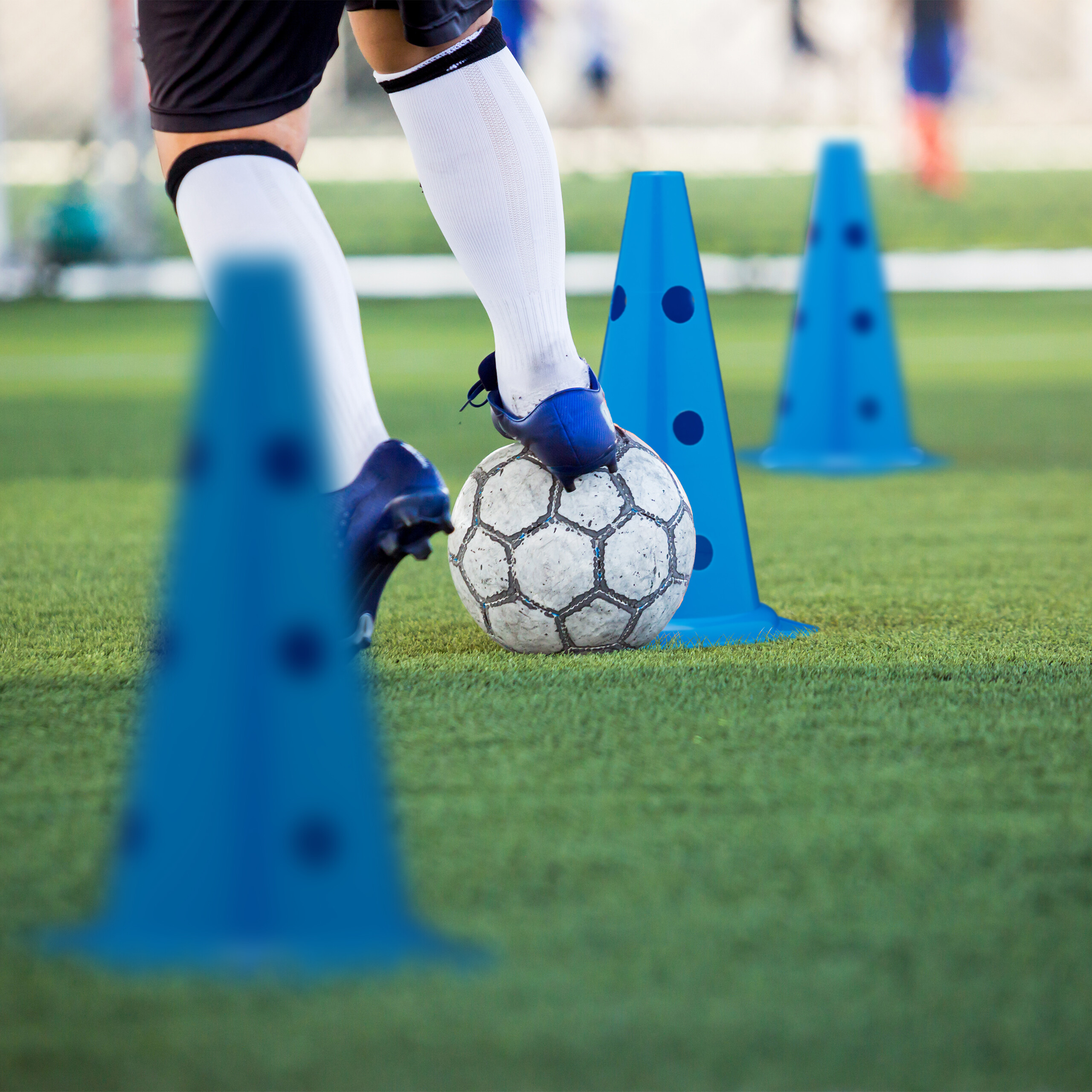 Ein Fußballspieler übt Dribbling mit blau-schwarzen Hütchen auf einem Rasen.