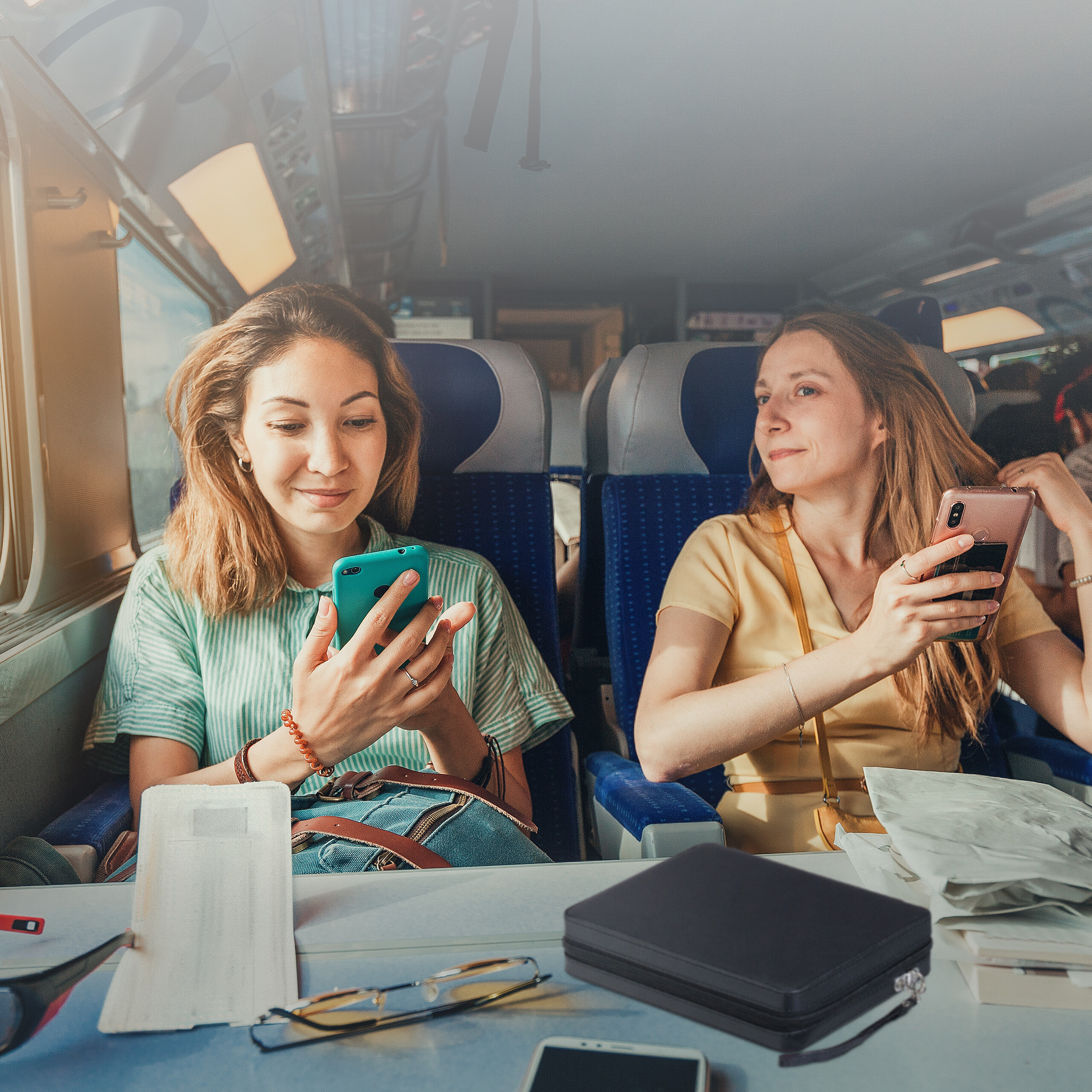 Zwei Frauen sitzen im Zug, schauen auf ihre Smartphones und lächeln während der Reise.