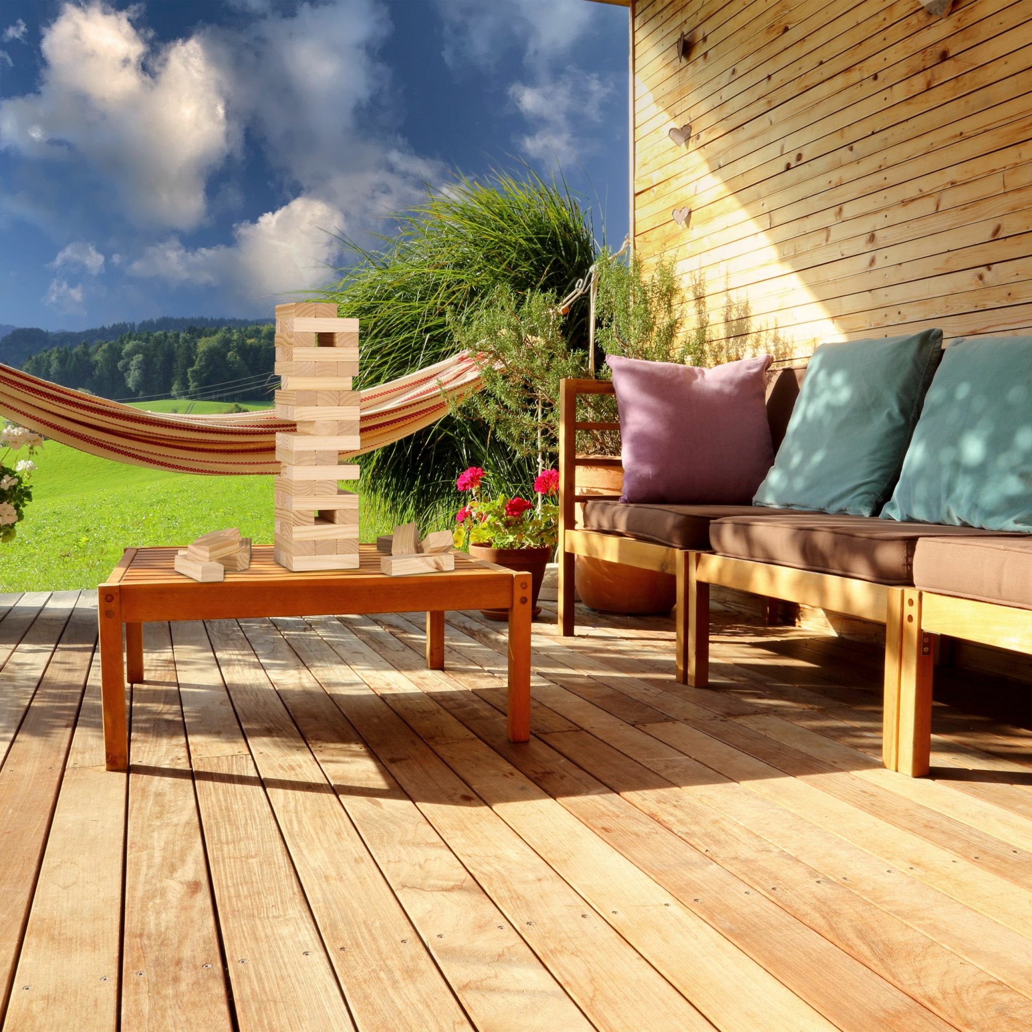 Eine Holzterrasse mit Turmspiel auf einem Tisch, Sofa mit Kissen, Hängematte und grünem Tal im Hintergrund.
