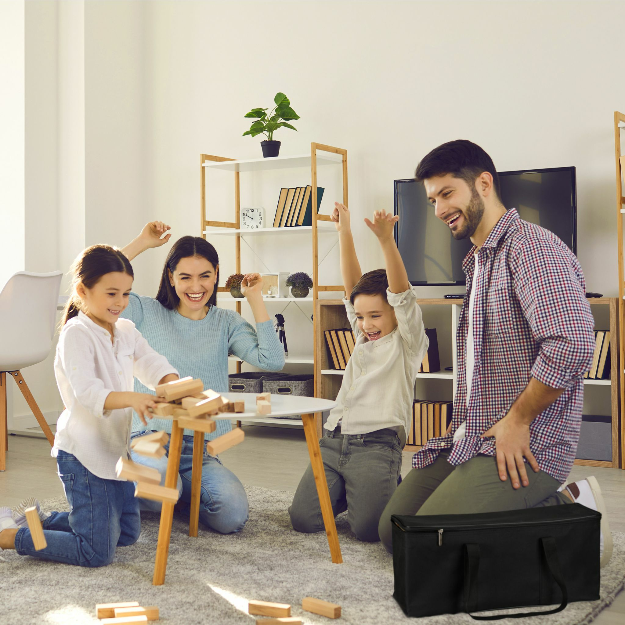 Eine glückliche vierköpfige Familie spielt in einem hellen Wohnzimmer und jubelt, als der Turm umfällt.