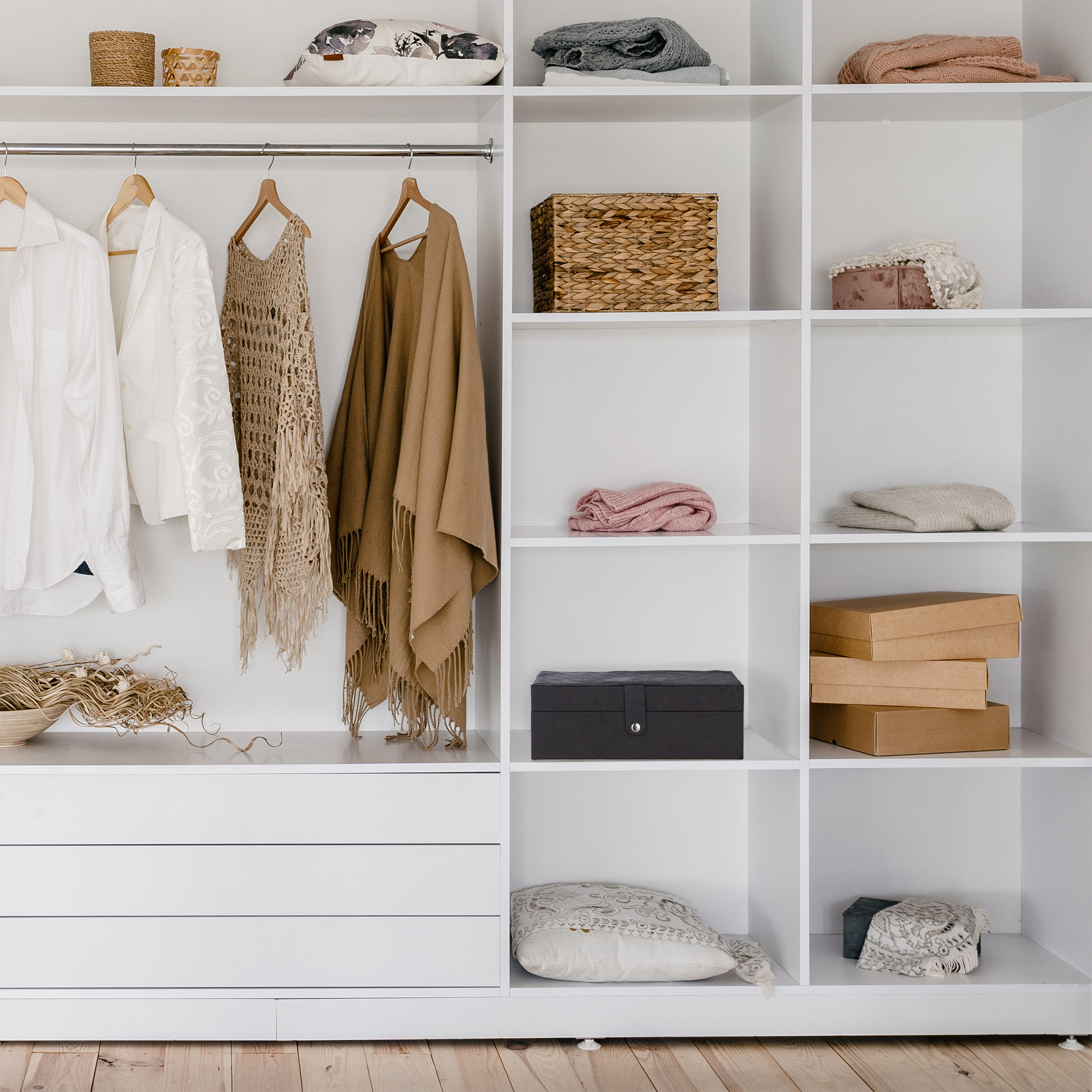 Ein weißer Kleiderschrank mit Hängekleidung, gefalteten Pullovern, dekorativen Kissen und Aufbewahrungsboxen.