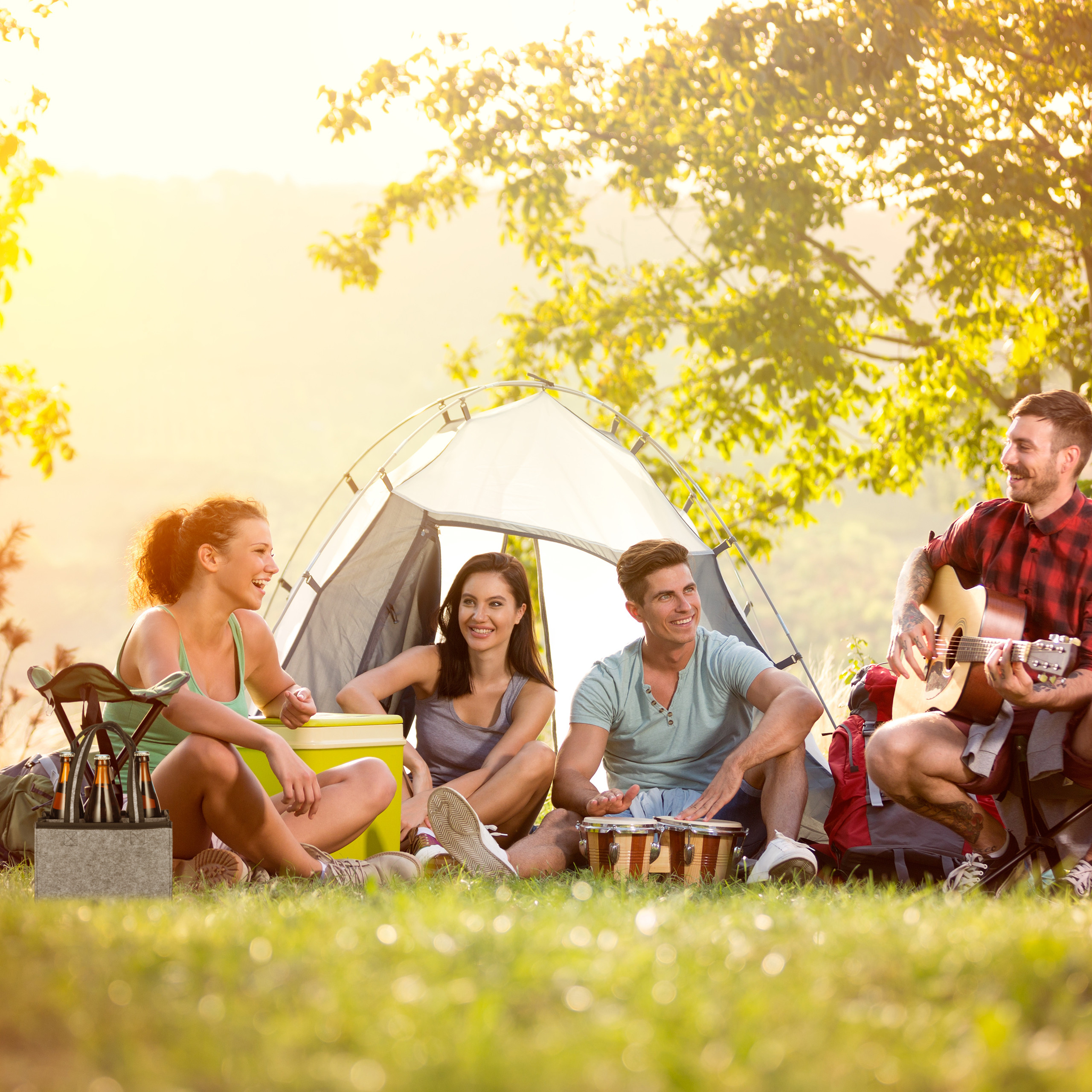 Freunde beim Camping, spielen Gitarre und Trommeln am Zelt bei Sonnenuntergang.