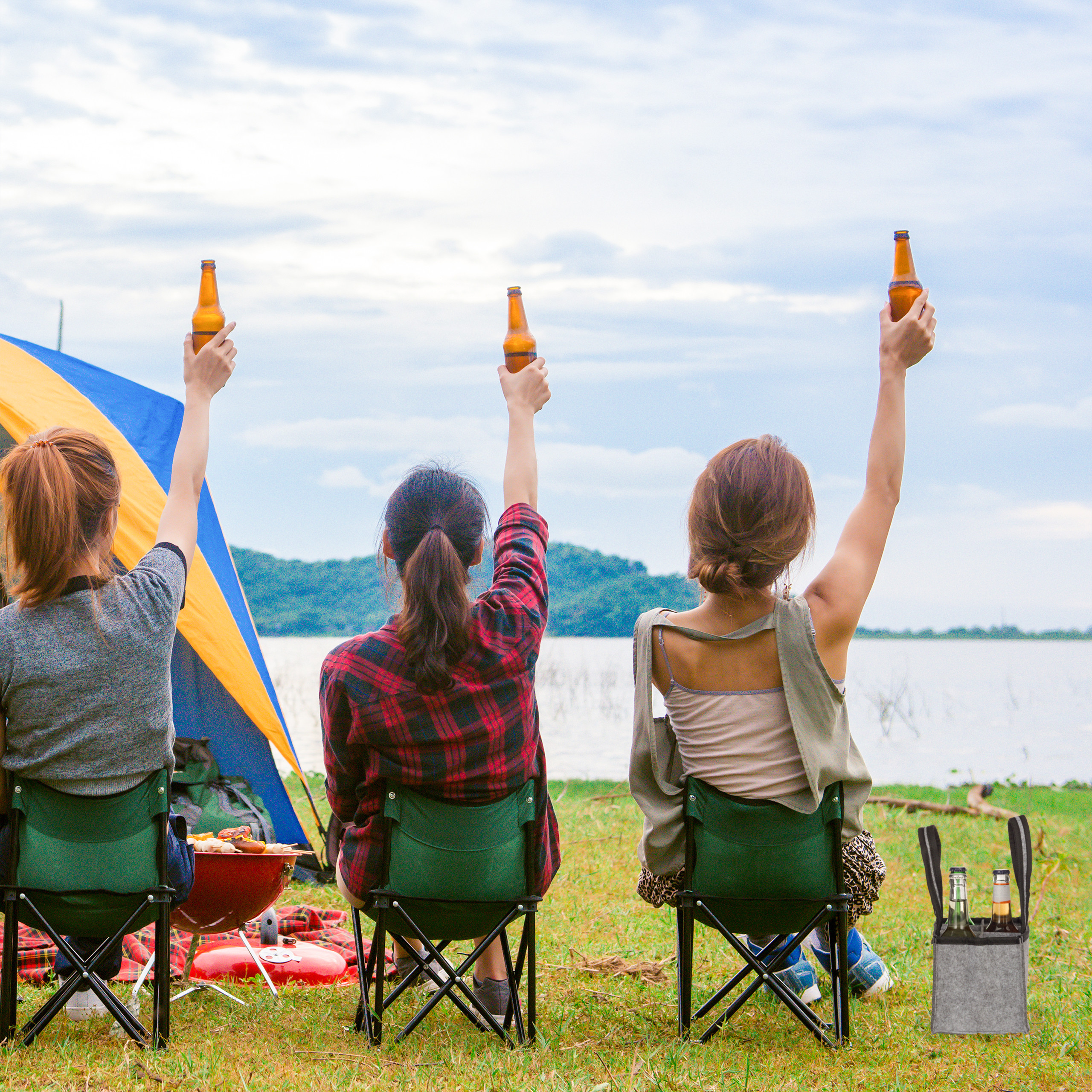 Drei Frauen sitzen am See in Campingstühlen und halten Flaschen in die Höhe.