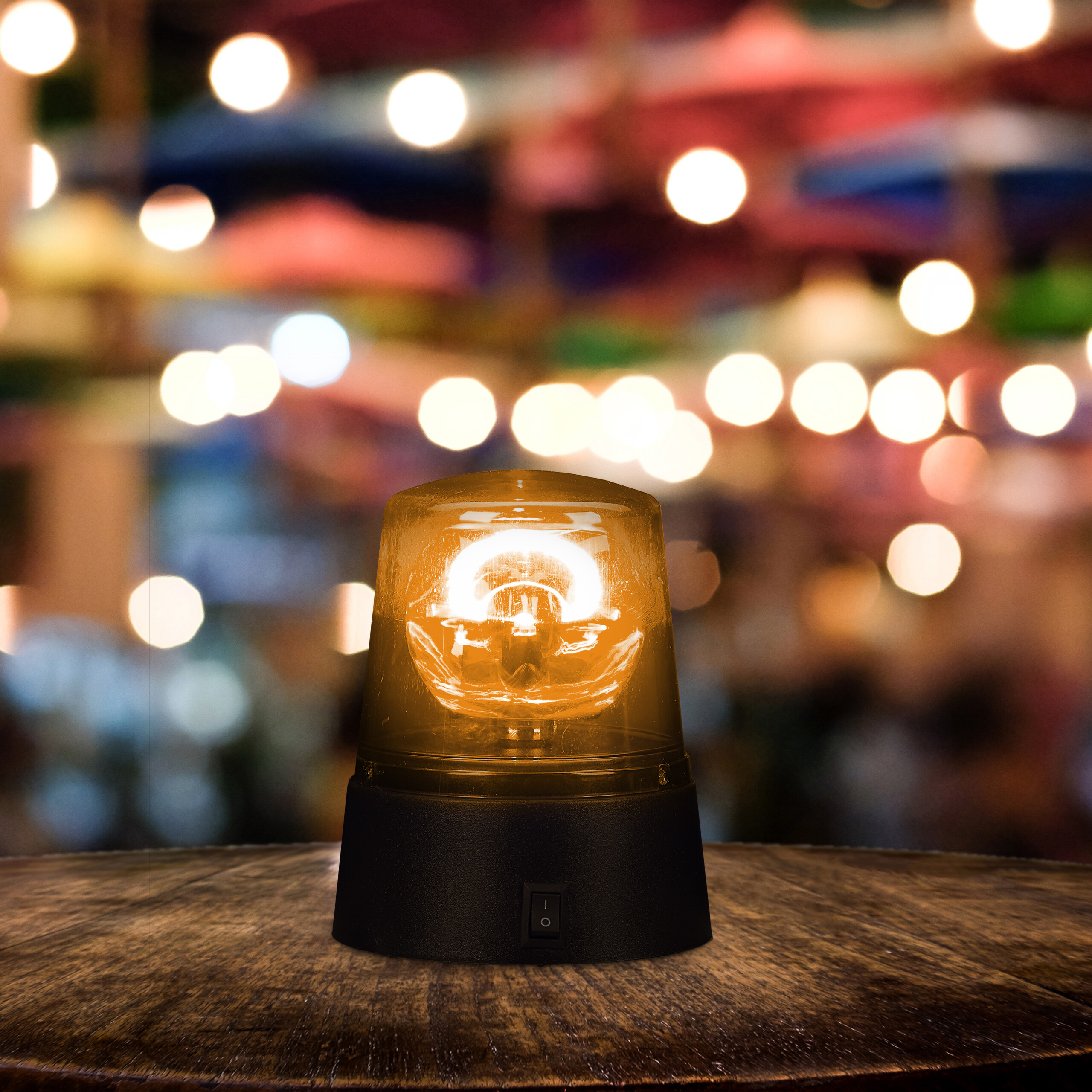 Ein beleuchtetes gelbes Warnlicht mit schwarzem Sockel steht auf einem Holztisch, im Hintergrund Bokeh-Lichter.