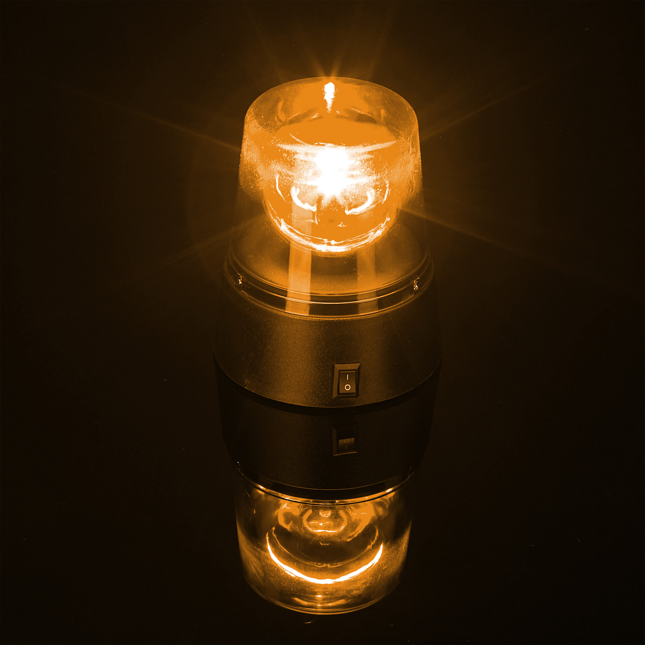 Eine leuchtende orangefarbene Warnleuchte mit schwarzer Basis und Schalter auf schwarzem Hintergrund.