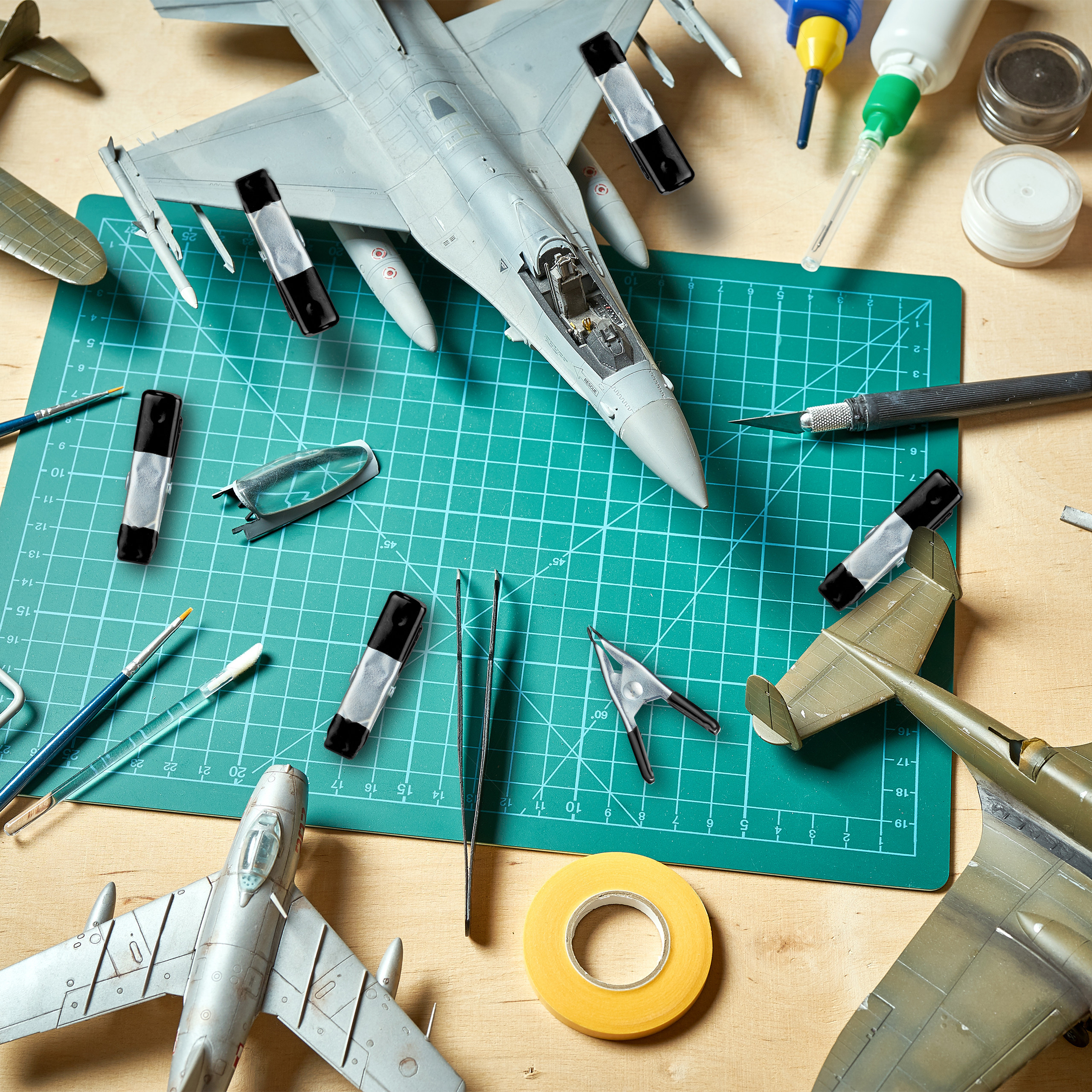 Modellbau-Werkstatt mit unvollständigen Flugzeugmodellen, Klemmen und Werkzeugen auf grüner Schneidematte.