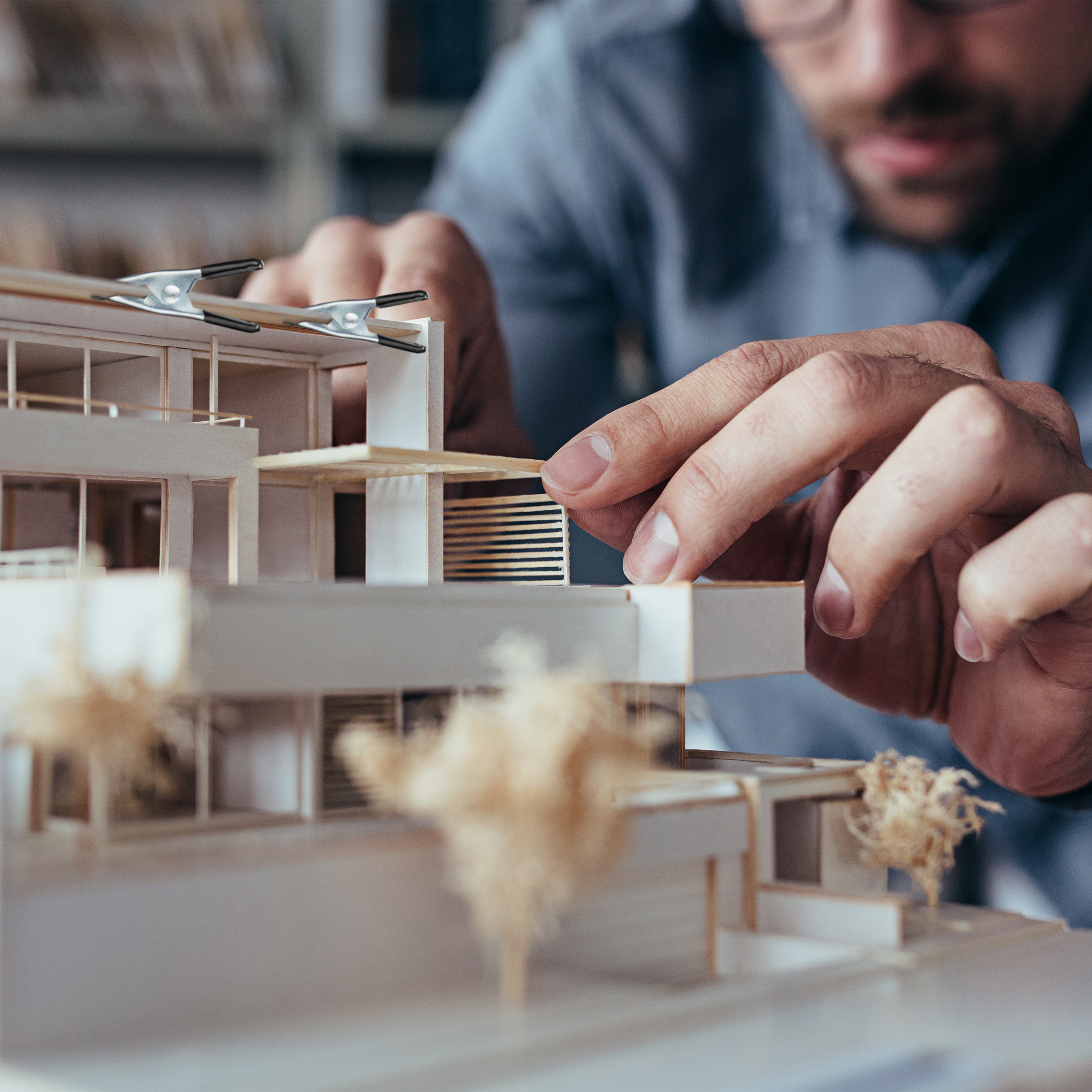 Ein Architekt arbeitet detailverliebt an einem modernen Architekturmodell mit kleinen Bäumen.