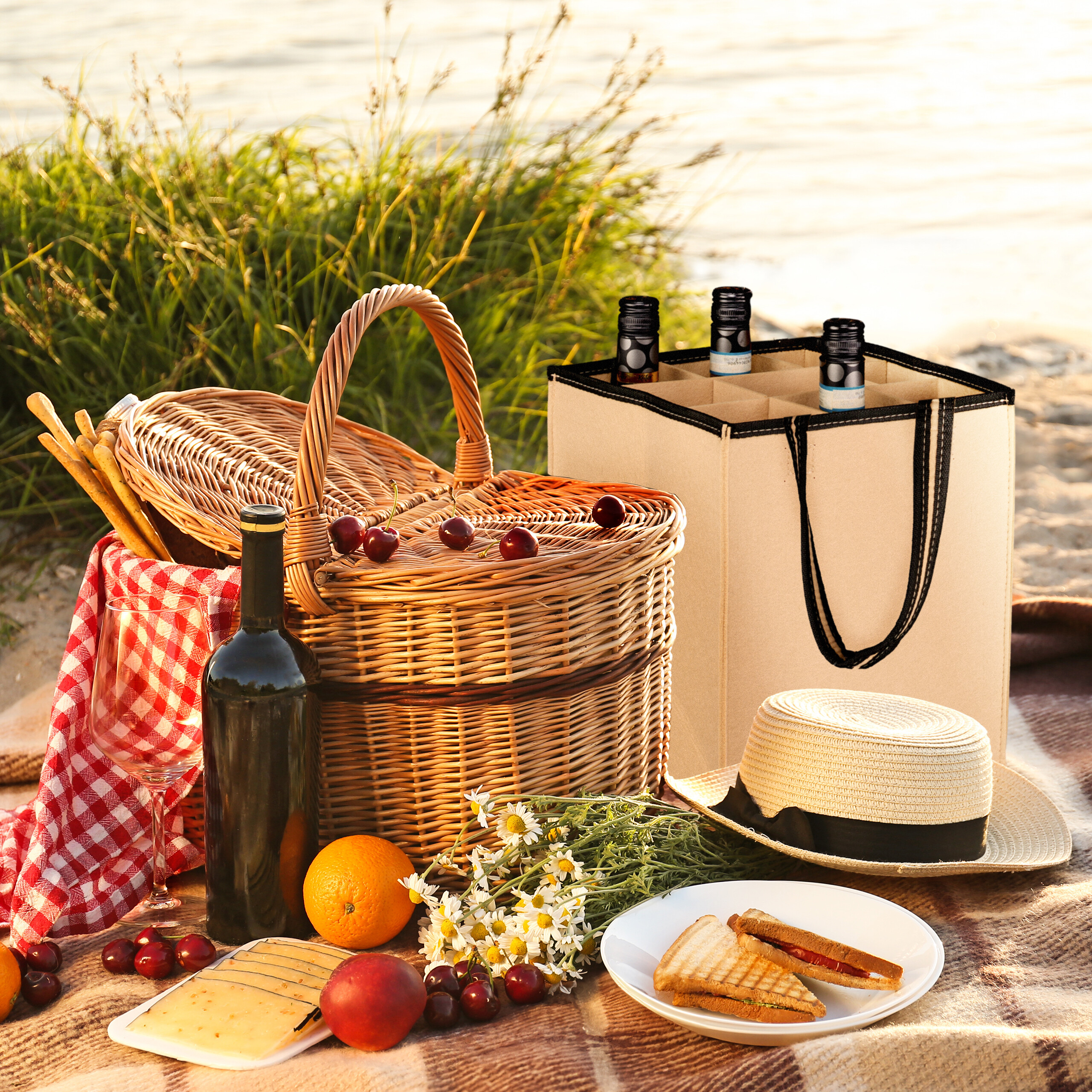 Ein Picknickkorb, Wein, Sandwiches, Kirschen und Blumen auf einer Decke im Freien.