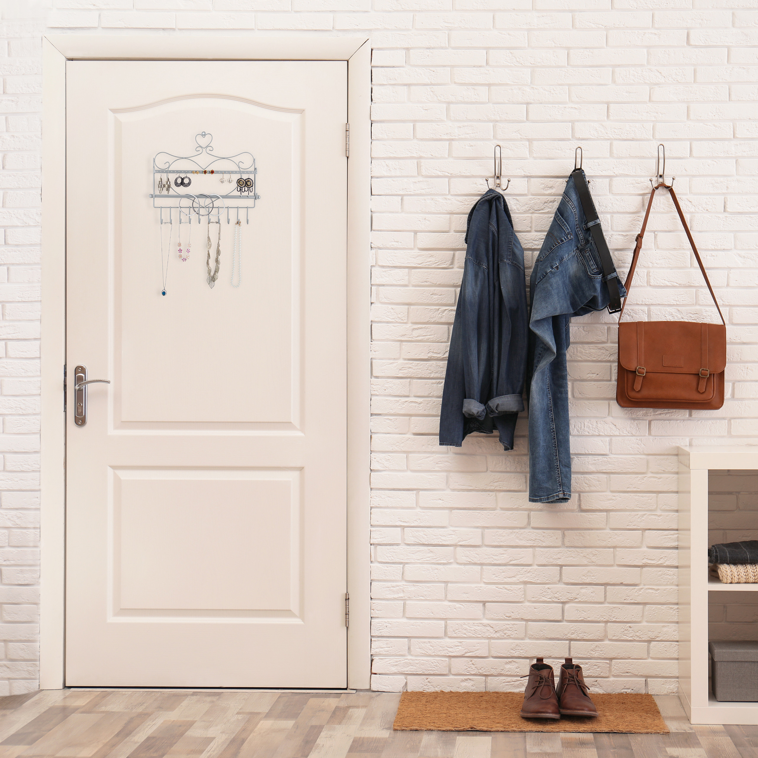Weiße Tür mit Schmuckhalter, Jacke, Jeans und brauner Tasche an einer weißen Backsteinwand, dazu Schuhe auf einer Fußmatte.