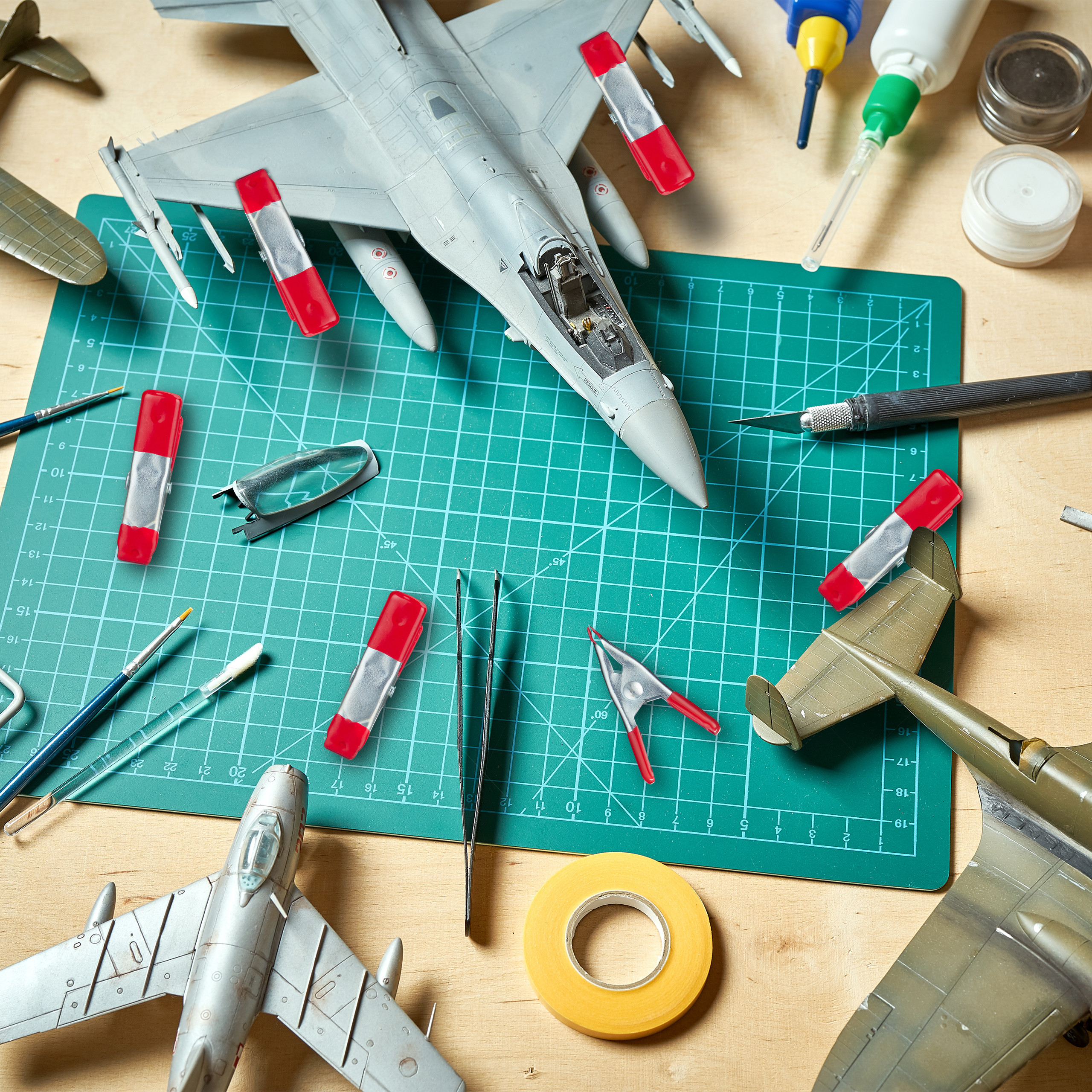 Modellflugzeugteile, Kleber und Werkzeuge auf einer grünen Schneidematte und Holztisch.