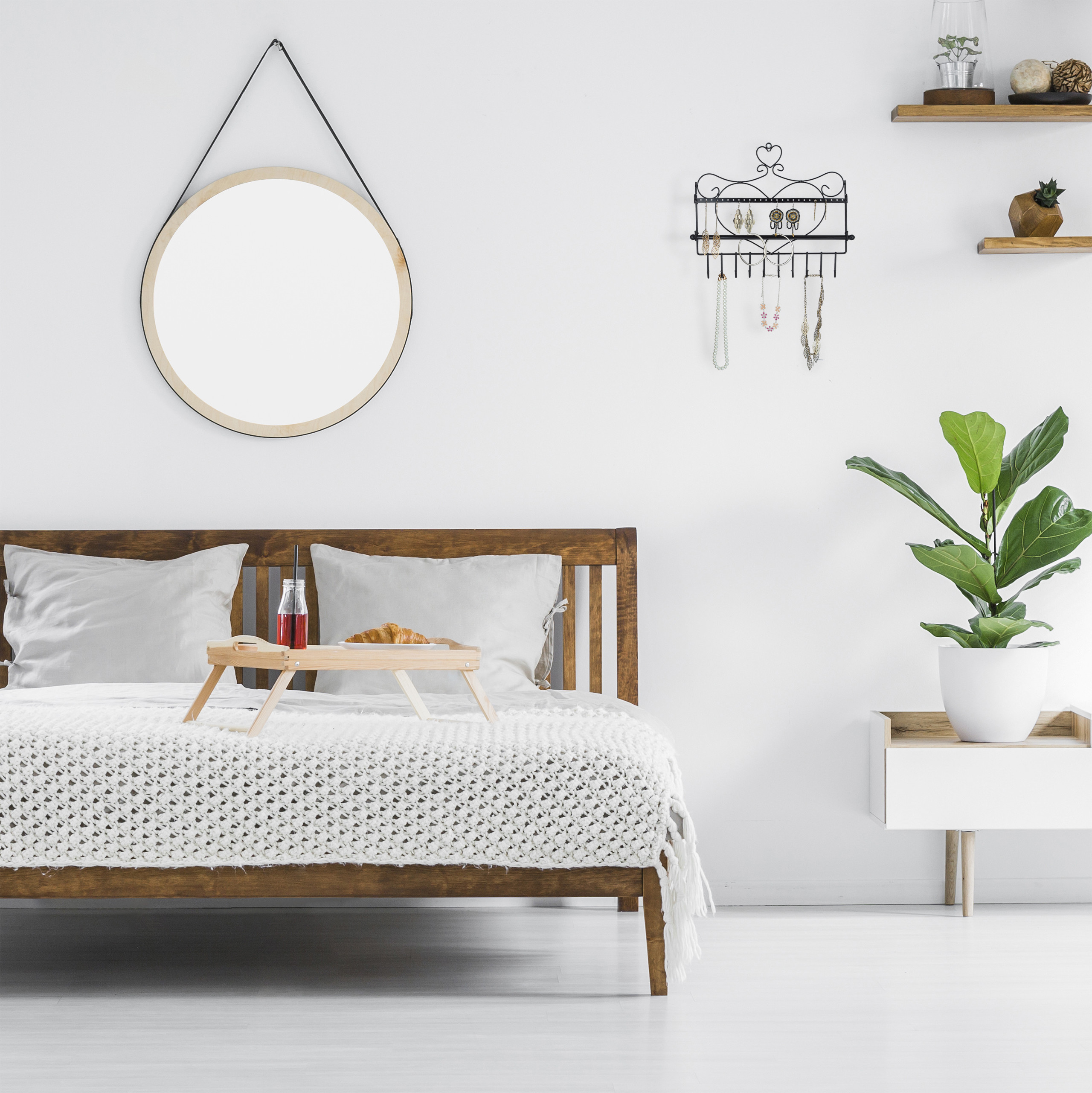 Gemütliches Schlafzimmer mit Holzbett, Frühstückstablett, rundem Spiegel und Topfpflanze an weißer Wand.