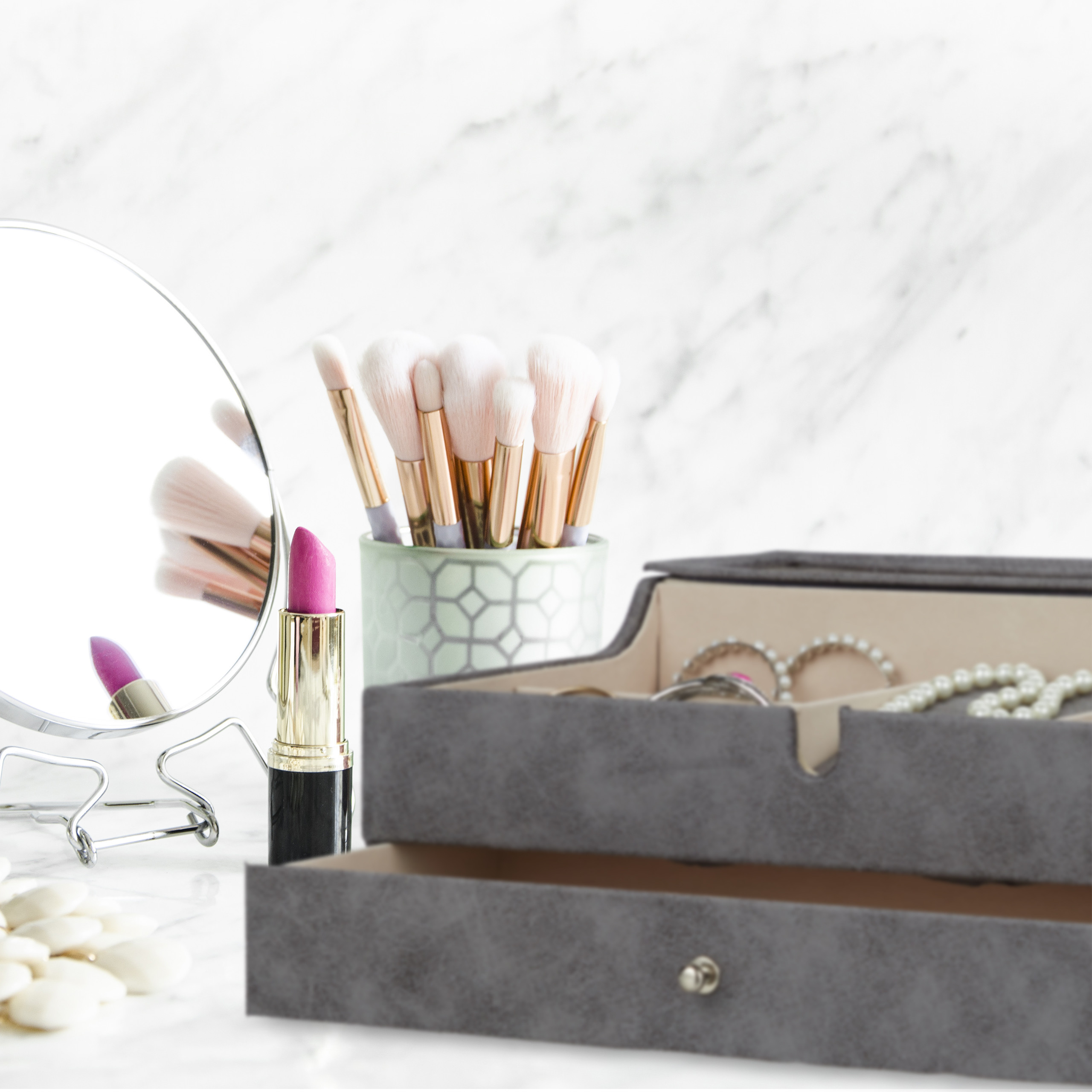 Make-up-Pinsel, Lippenstift, ein runder Spiegel und eine Schmuckschatulle auf einer Marmoroberfläche.