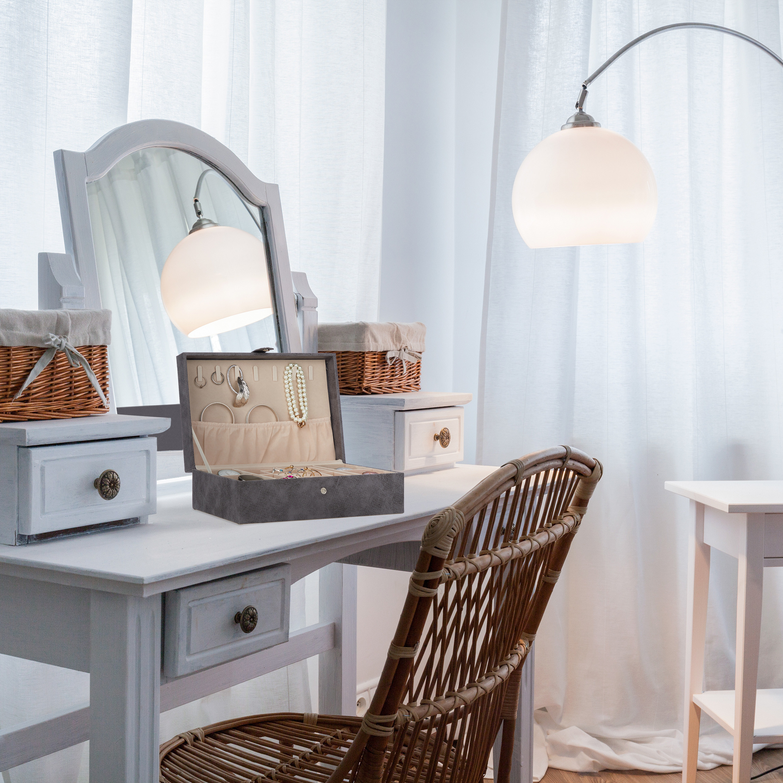Ein weißer Schminktisch mit Spiegel, offenem Schmuckkästchen, Körben und Rattan-Stuhl unter Lampe.
