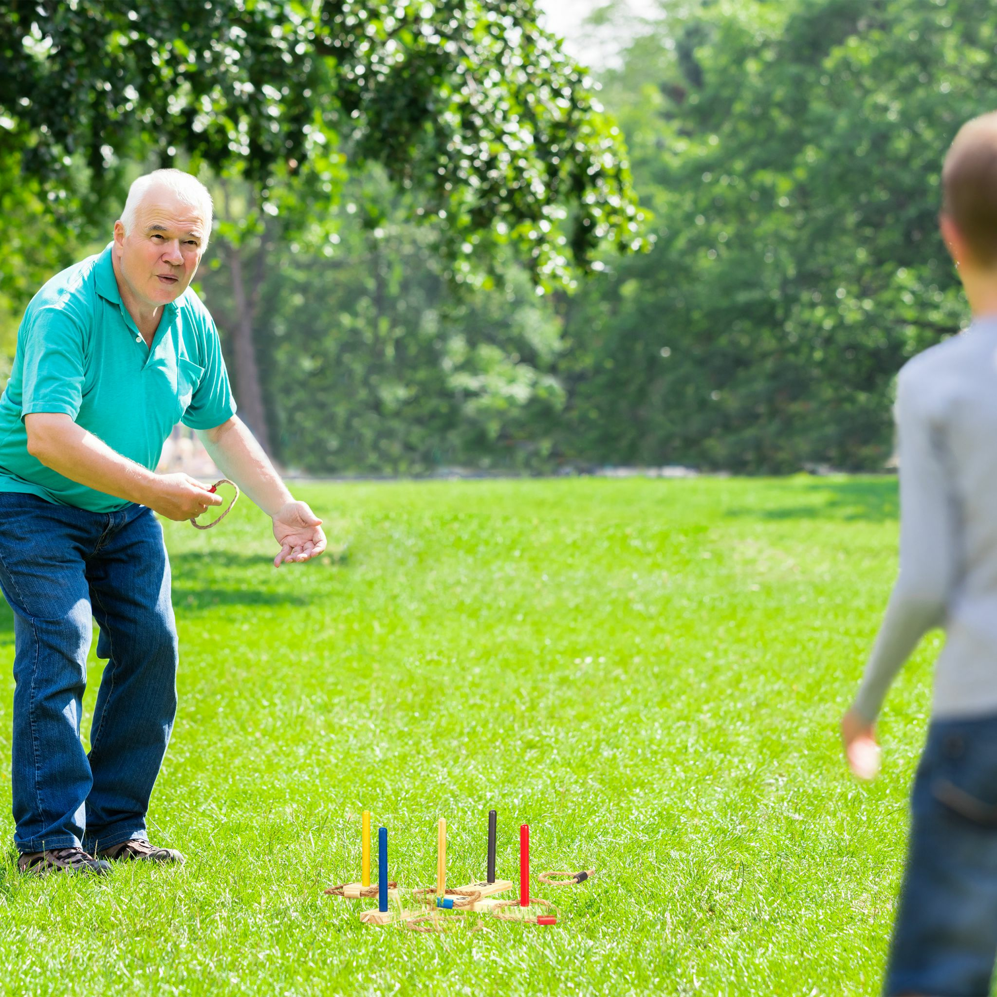 Älterer Mann spielt Ringwurfspiel im Park mit einem Jungen.