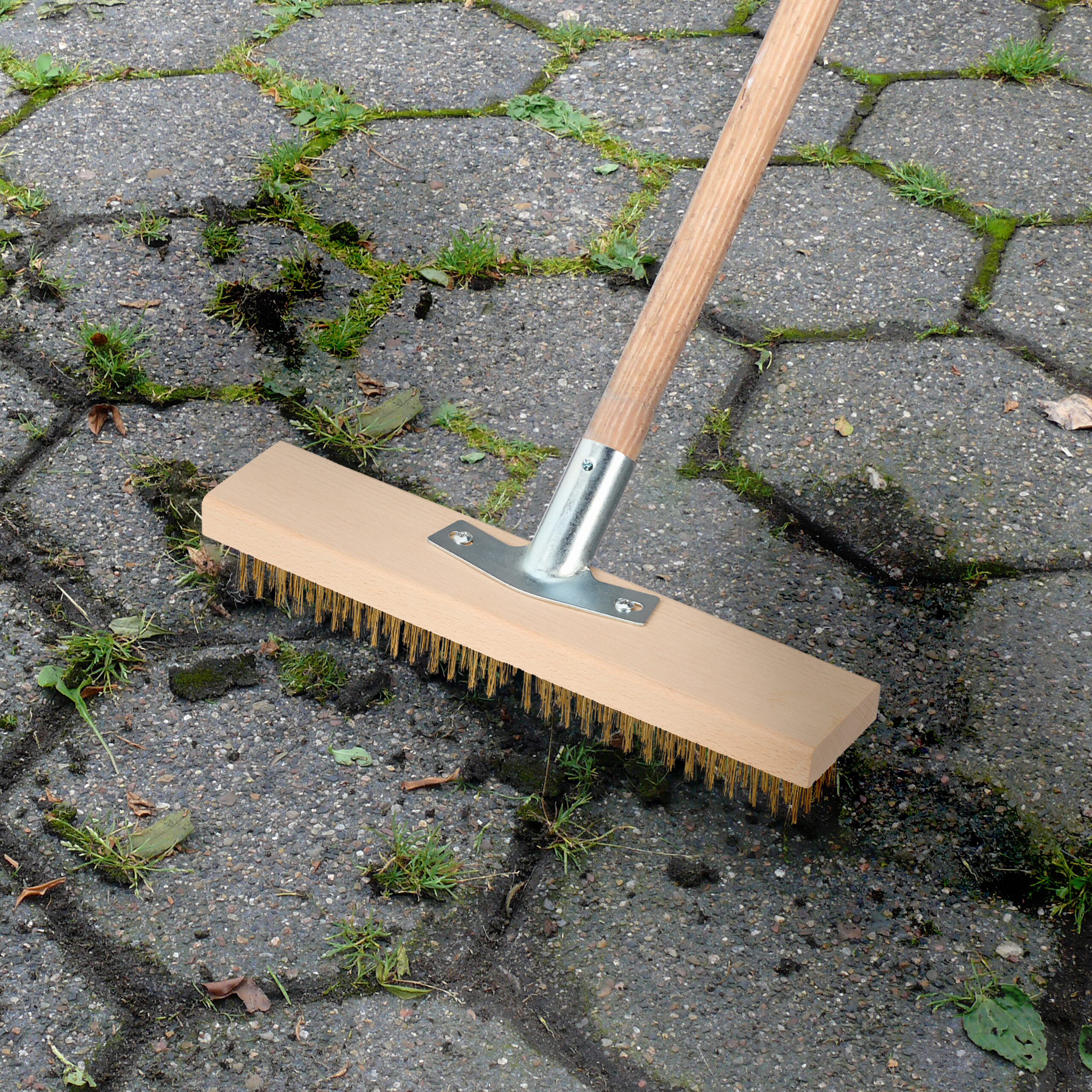 Ein Drahtbesen reinigt Unkraut zwischen grauen Pflastersteinen.