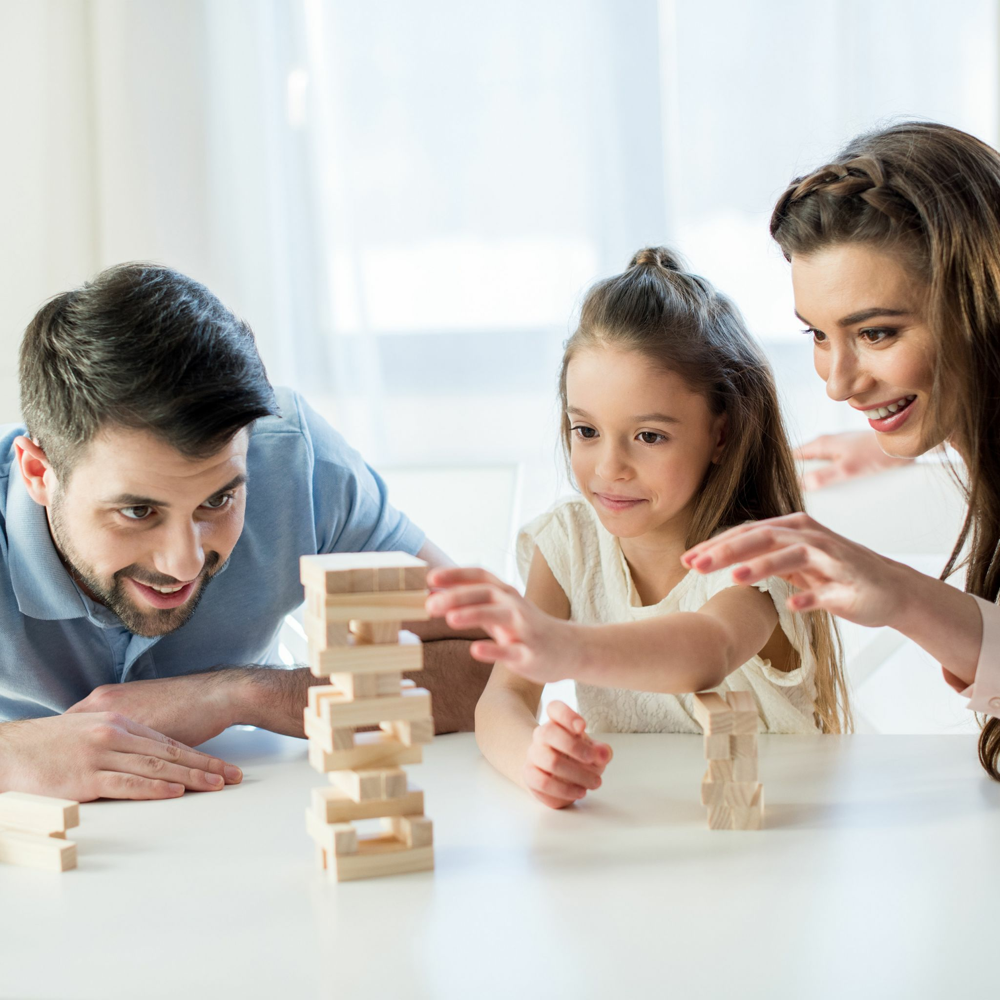Eine Familie spielt zusammen und baut einen Turm aus Holzklötzen an einem Tisch.