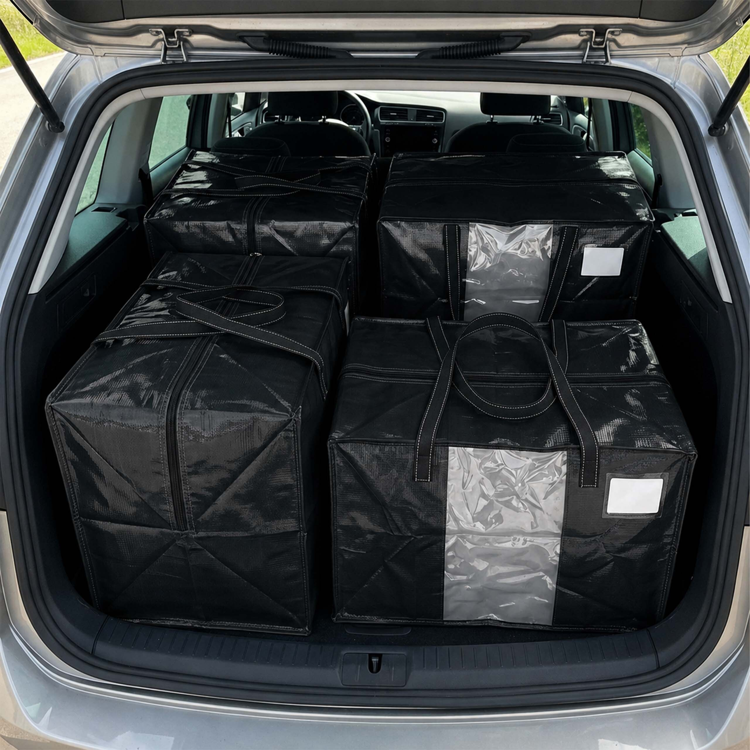 Vier große schwarze Aufbewahrungstaschen sind ordentlich im offenen Kofferraum eines silbernen Autos verstaut.