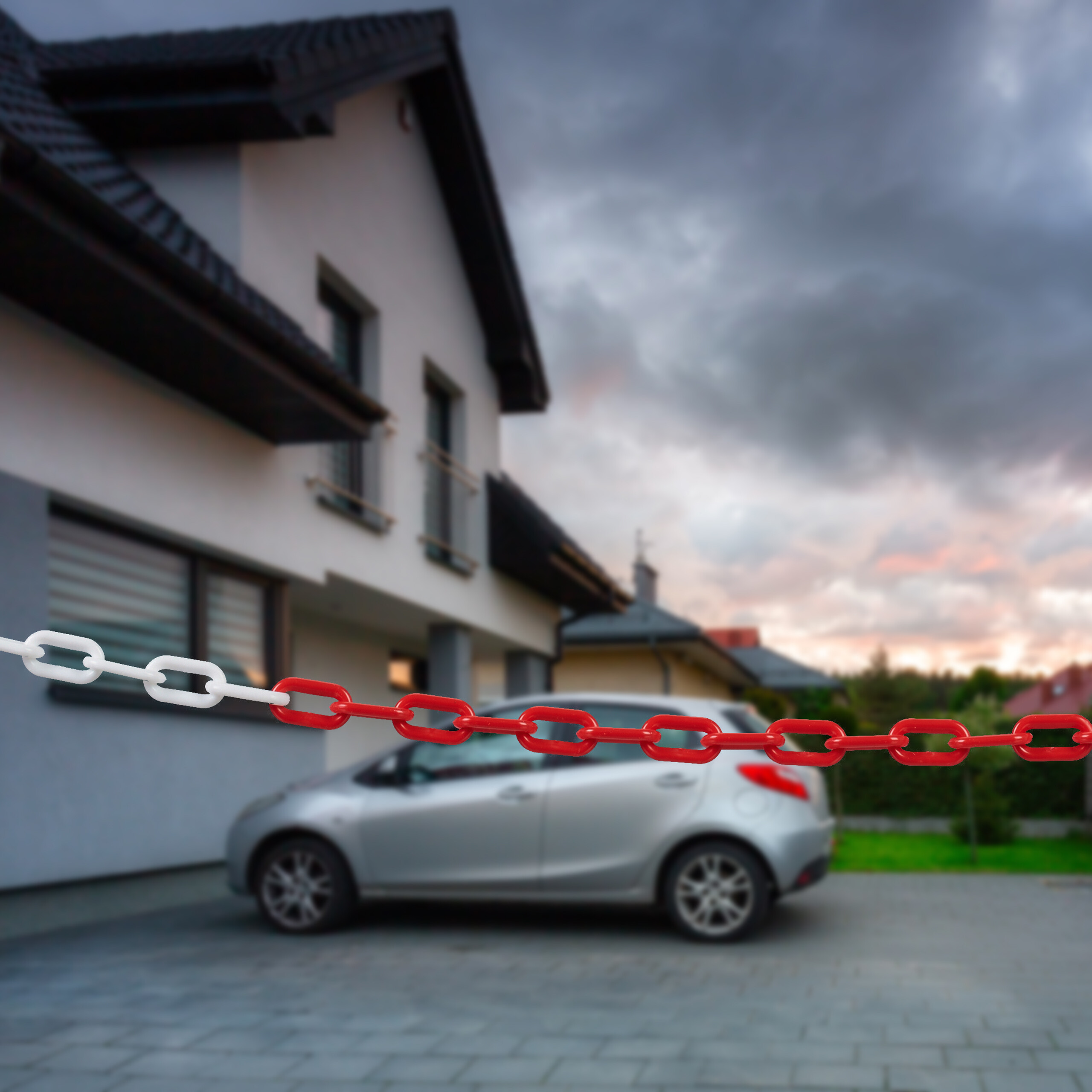 Eine rot-weiße Plastikkette sperrt ein modernes Haus und ein geparktes silbernes Auto unter bewölktem Himmel ab.
