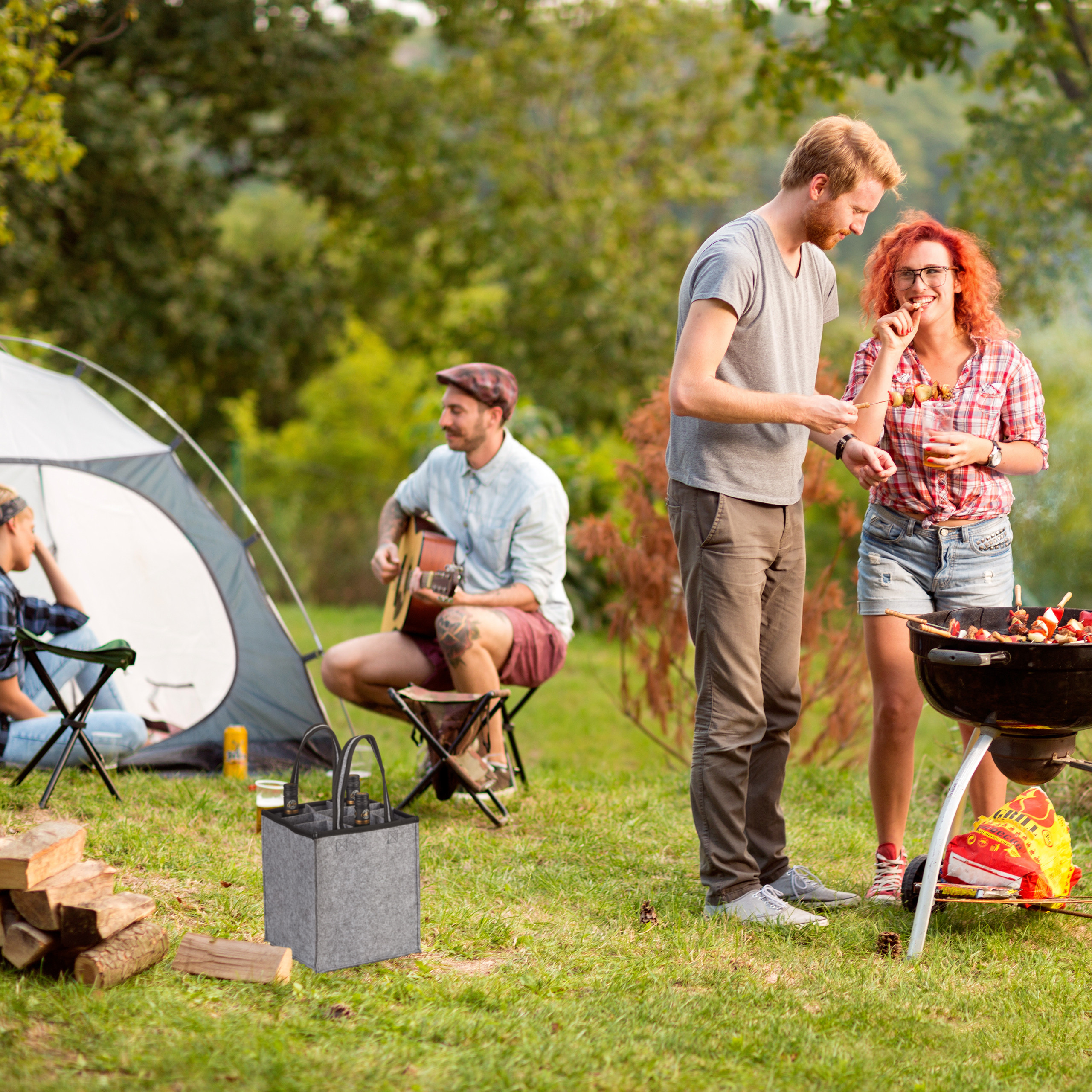 Freunde beim Camping, grillen, musizieren am Zelt und genießen Getränke aus einer Filztasche.