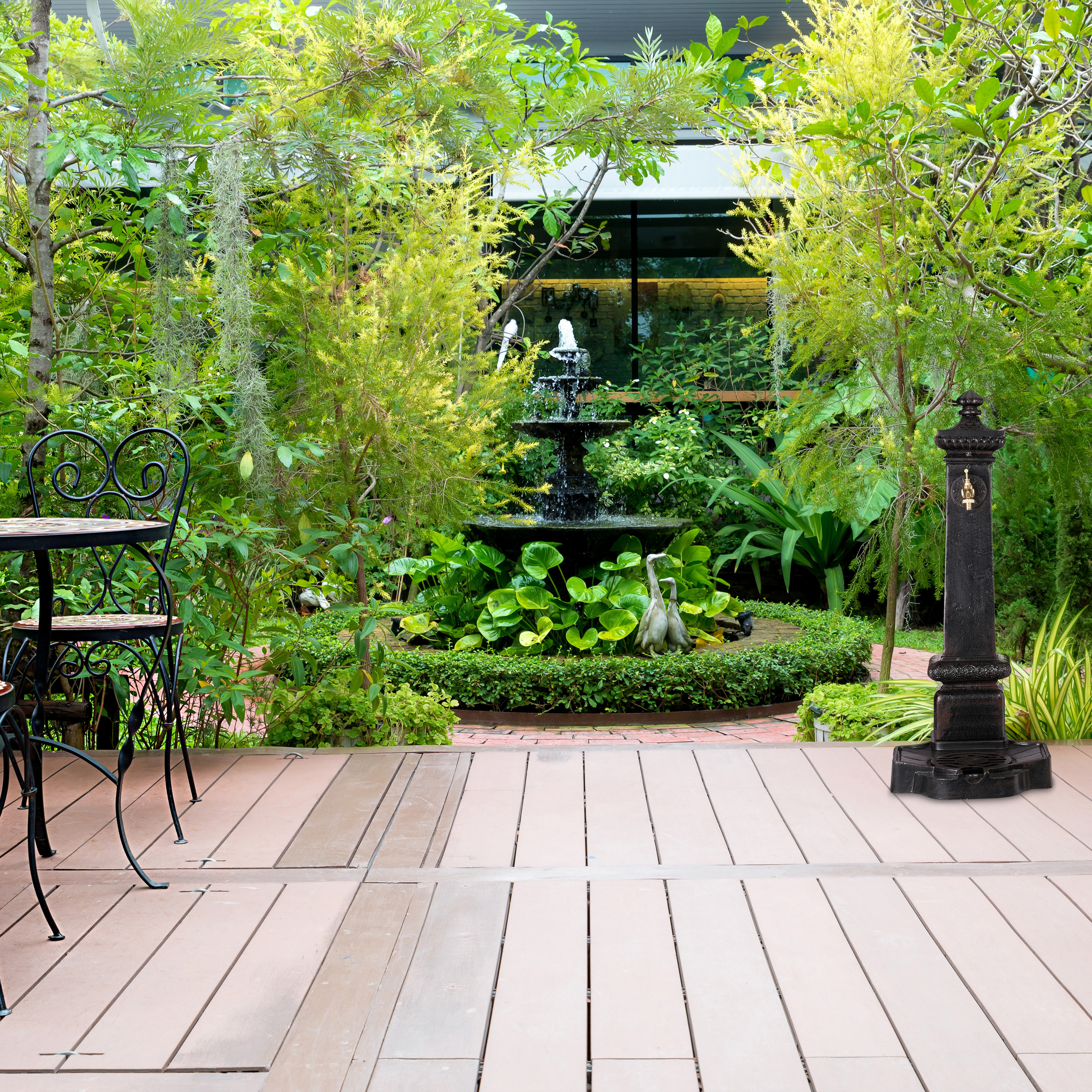 Ein Holzdachterrassengarten mit schwarzem Springbrunnen, viel Grün und einer dunklen Metallsäule.