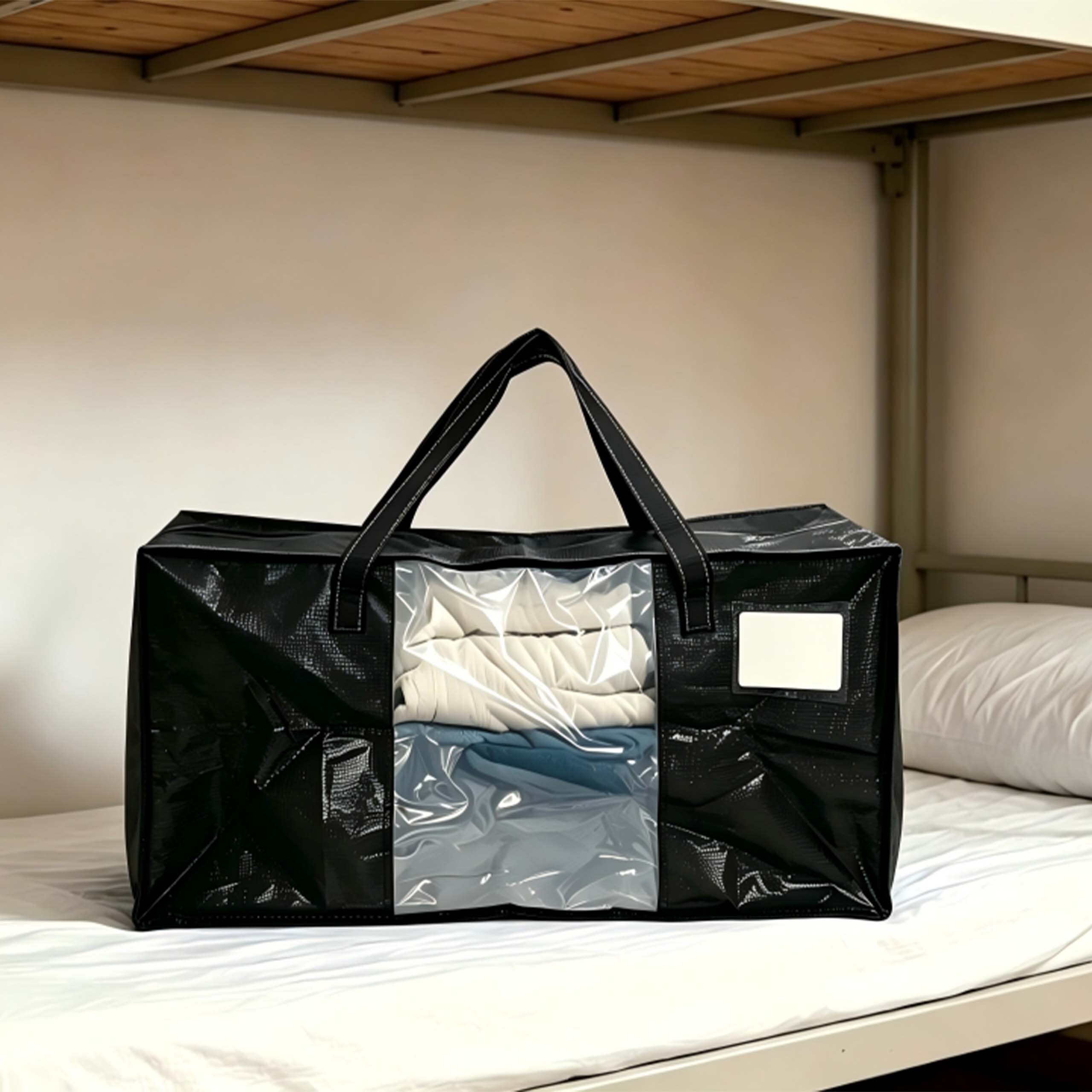Eine große schwarze Aufbewahrungstasche mit klarem Sichtfenster liegt gefüllt mit Kleidung auf einem Bett.