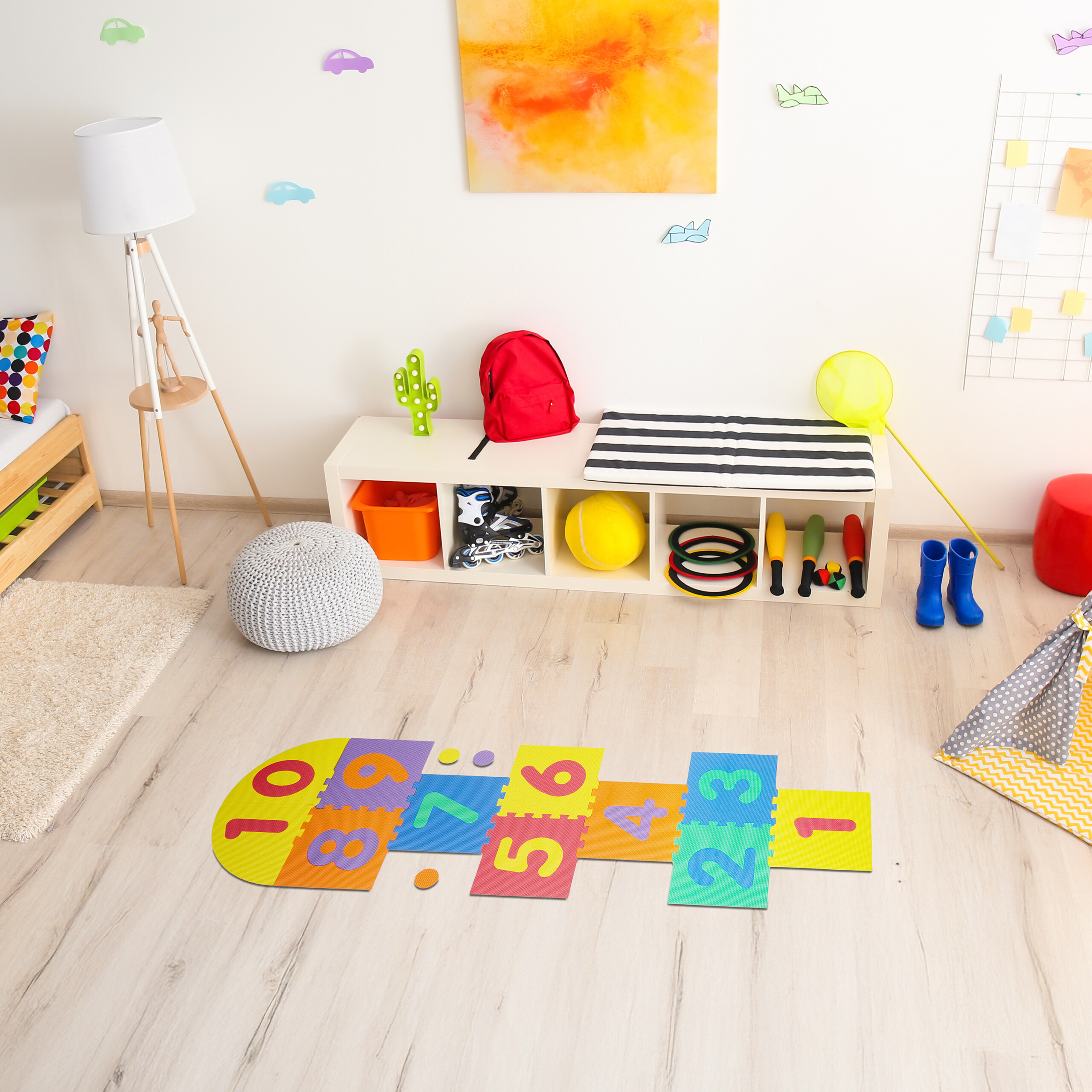 Buntes Kinderspielzimmer mit Kissen, Lampe, Spielzeugregal und einer bunten Hüpfmatte auf dem hellen Holzboden.