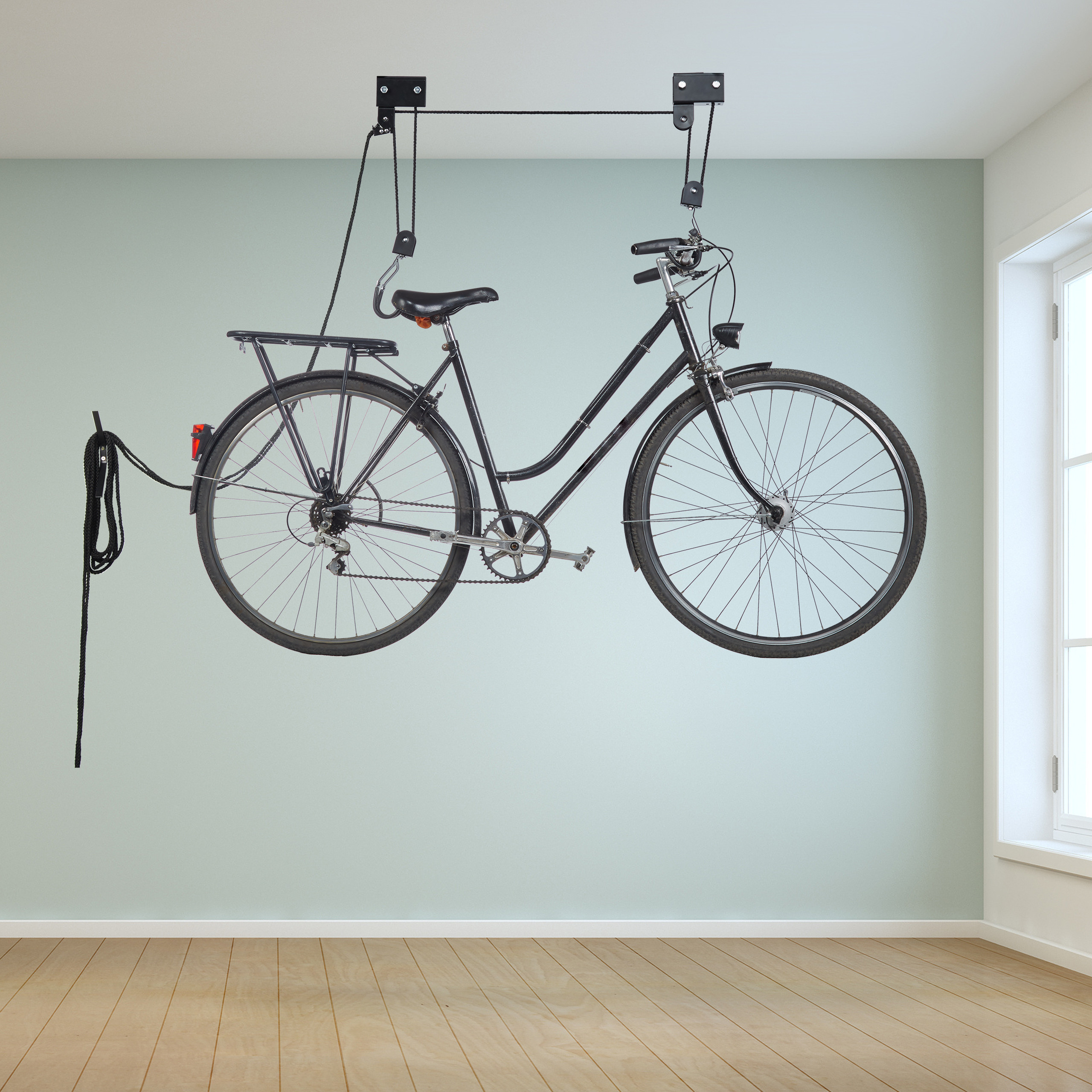 Ein schwarzes Fahrrad hängt an einem Deckenlift in einem Raum mit Holzboden und einer hellgrünen Wand.