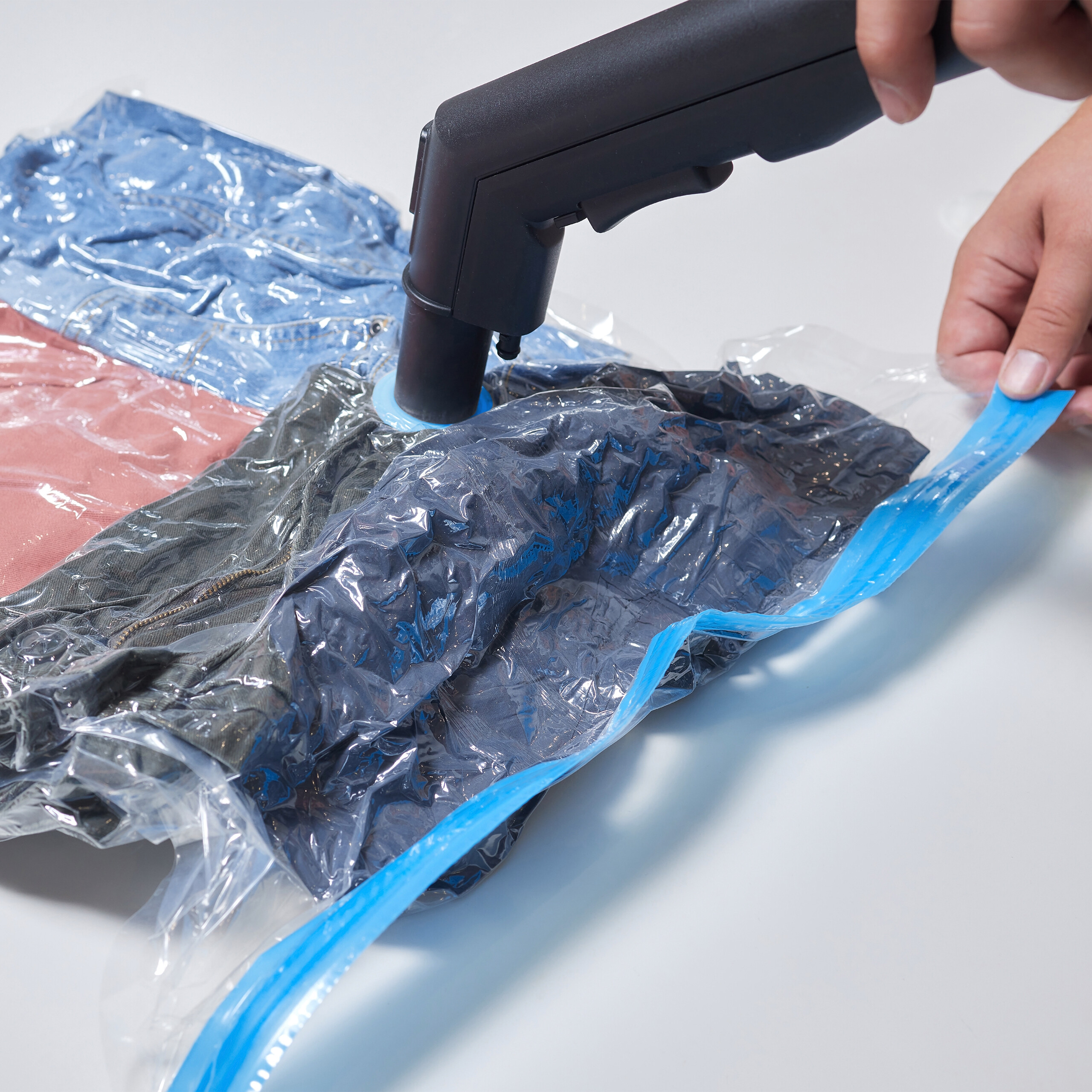 Ein Vakuumiergerät entfernt Luft aus einer Plastiktüte mit gefalteter Kleidung.